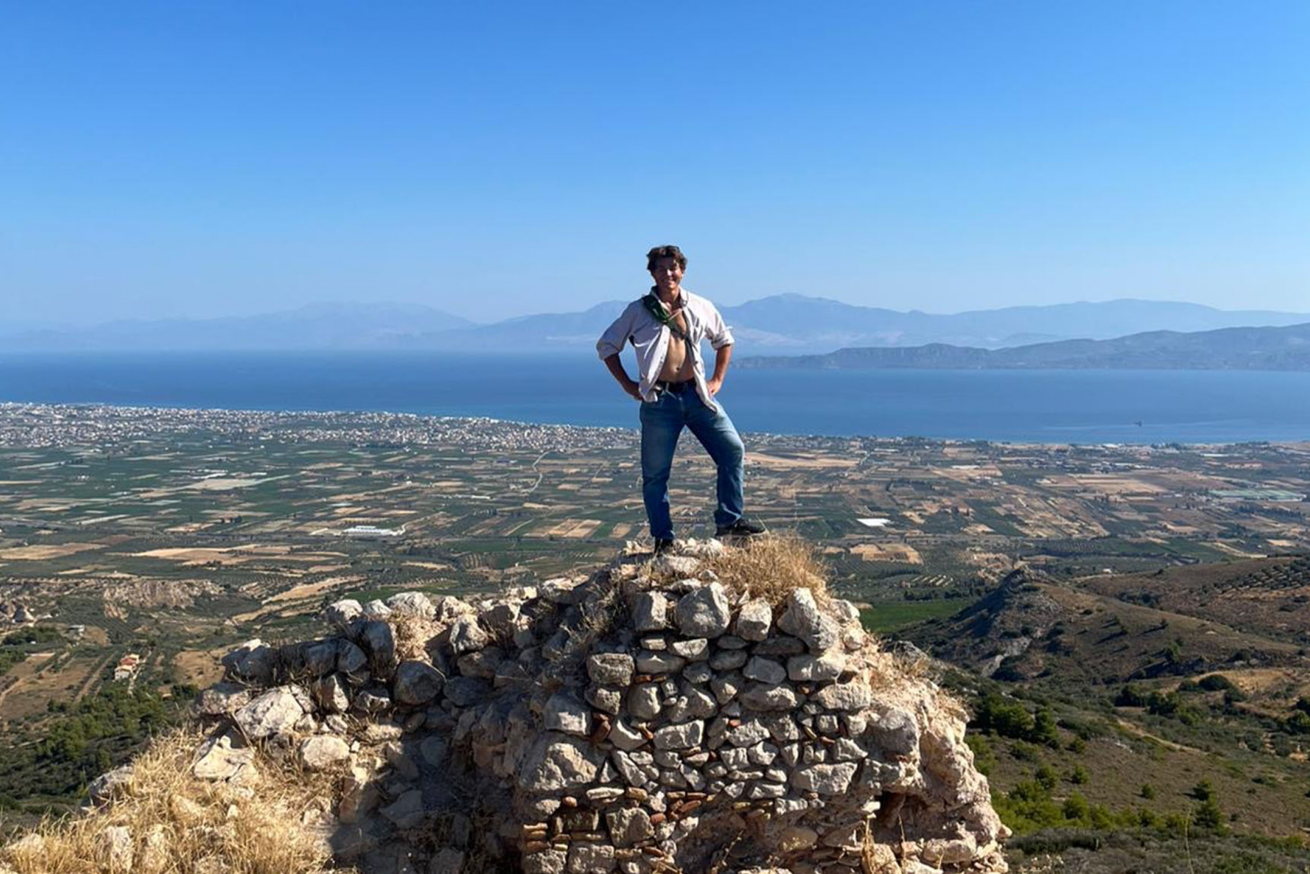 Person standing on top of a rock face, an entire city and mountains in the distance behind them.