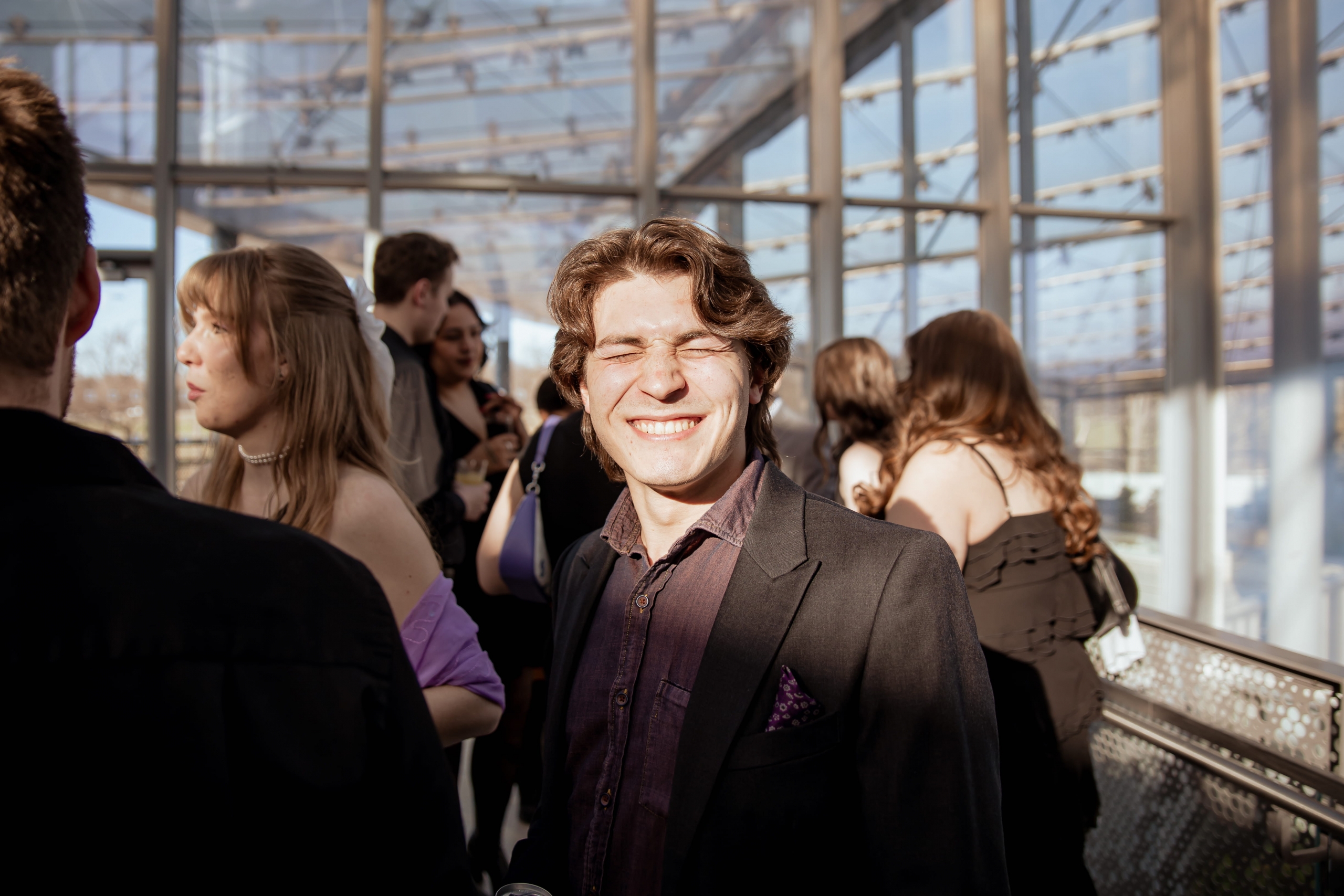 Person standing in a room with glass walls and ceiling, squinting their eyes from the sun.