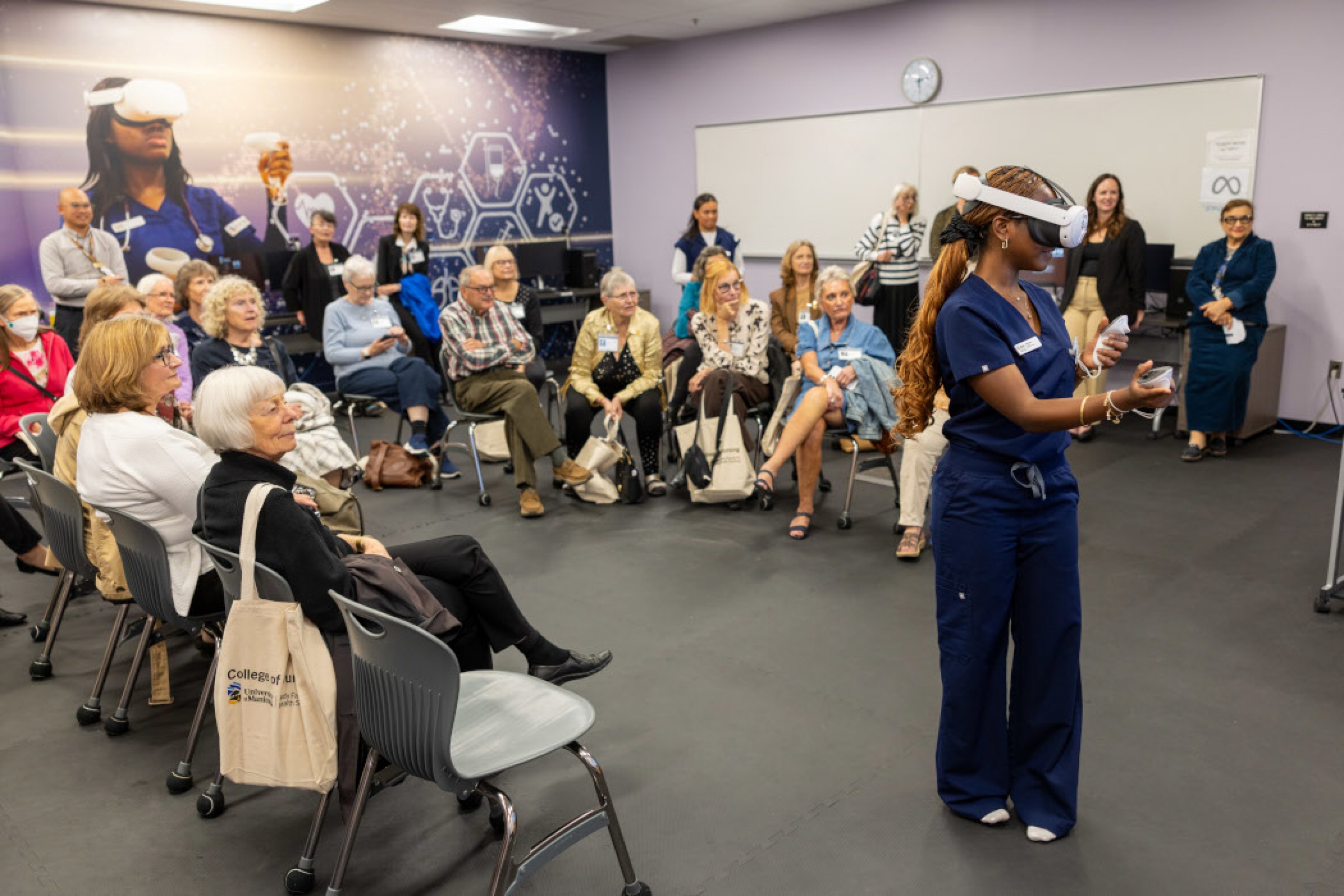 A nursing student demonstrates a virtual reality program in front of a room full of alumni. 