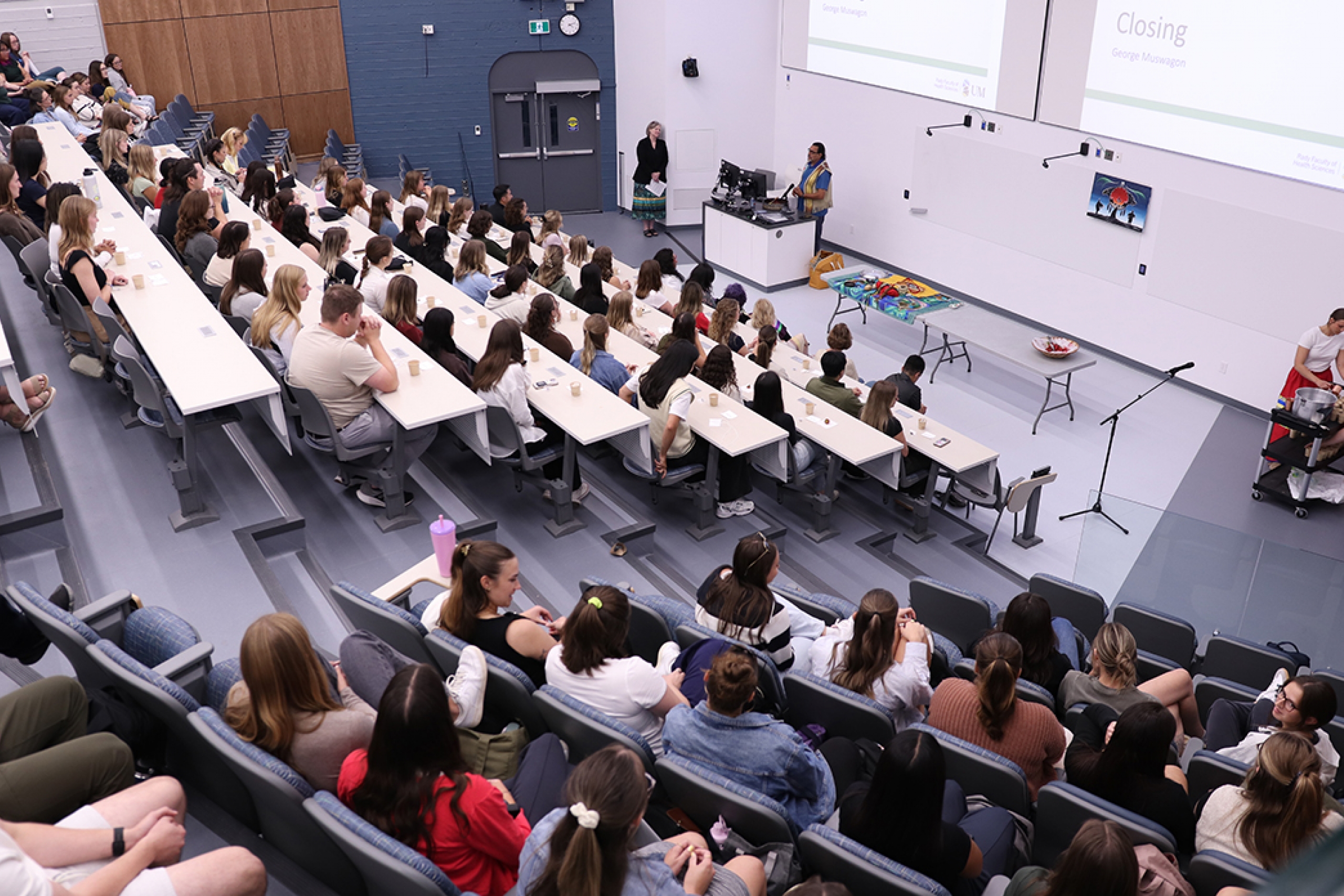 A large class of students at an Indigenous ceremony in a lecture hall.