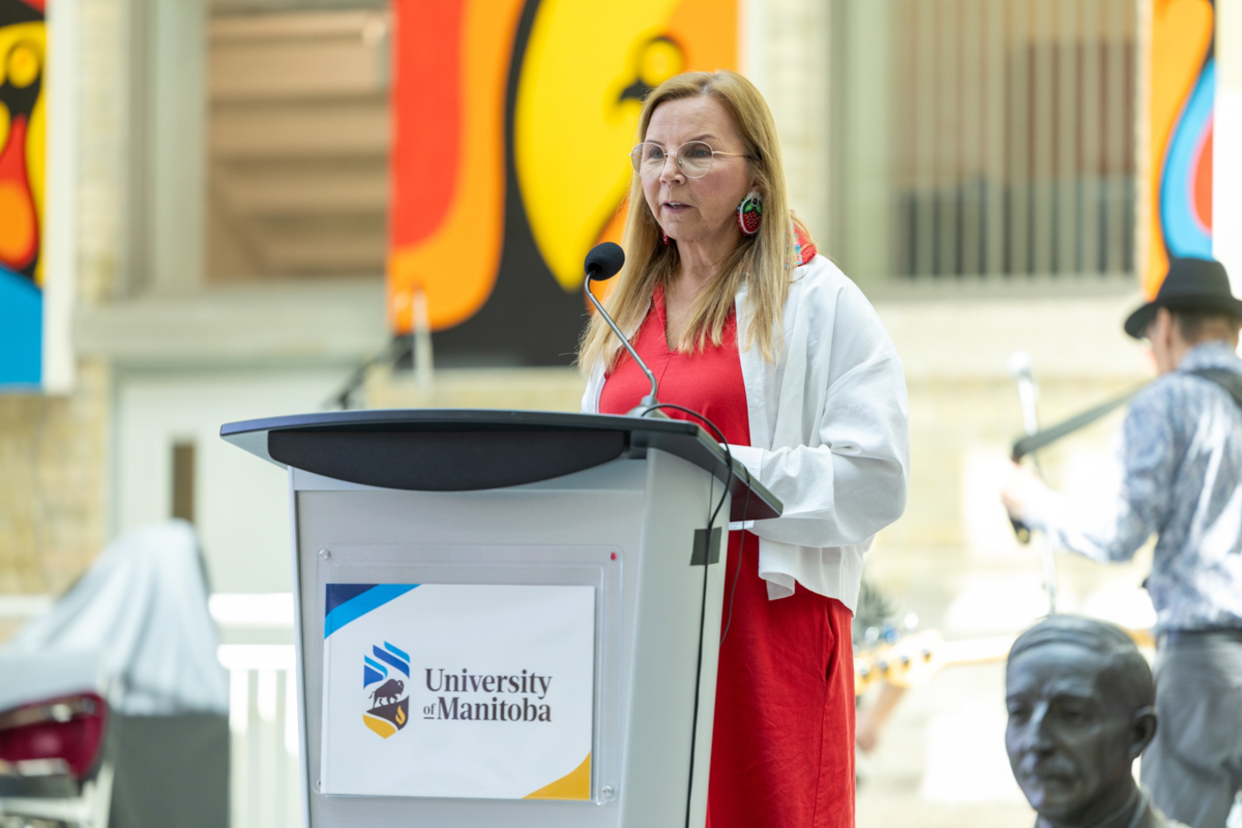 A person talks onstage behind a podium that has a logo of the University of Manitoba.