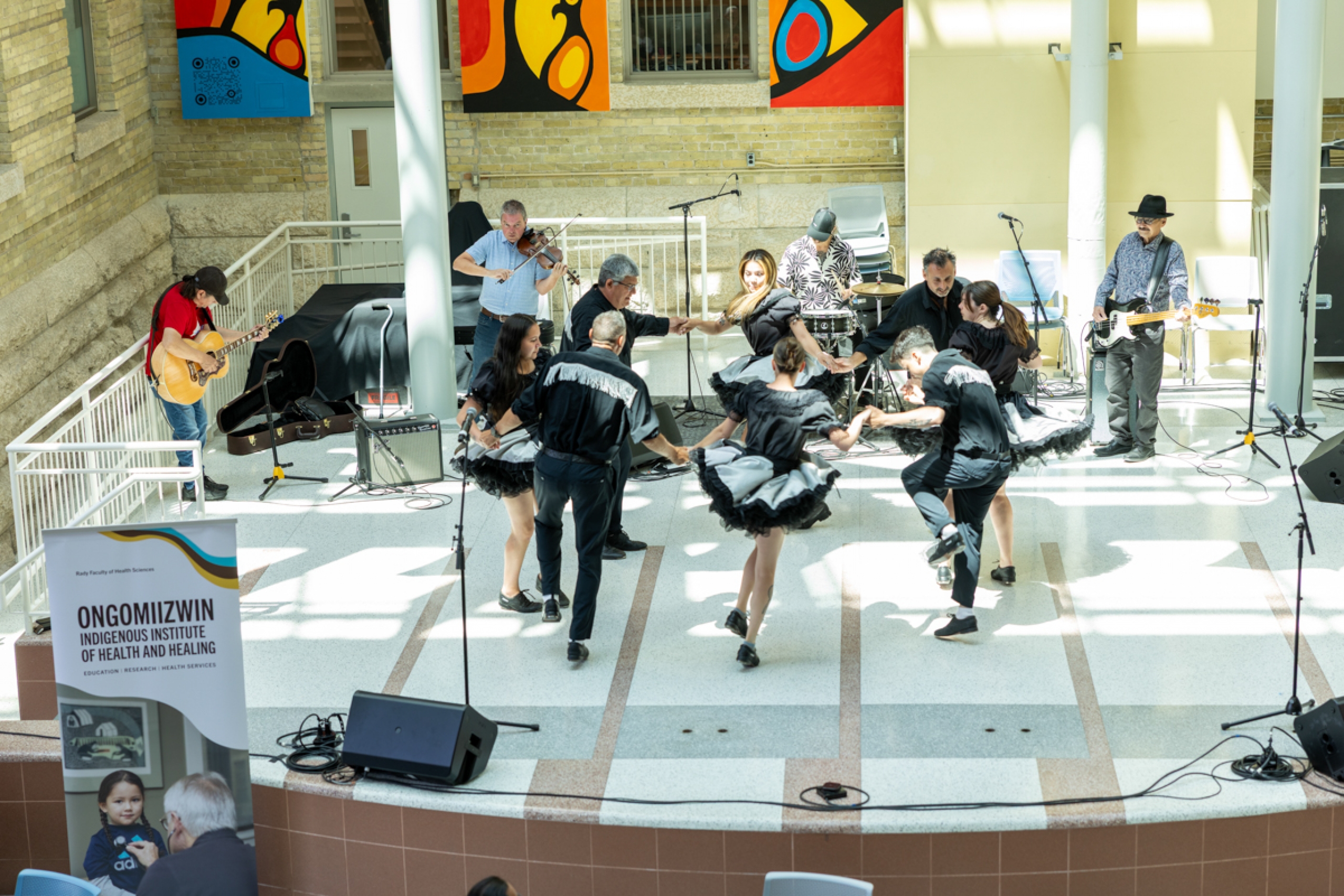A group of people dancing in a circle onstage with a band.