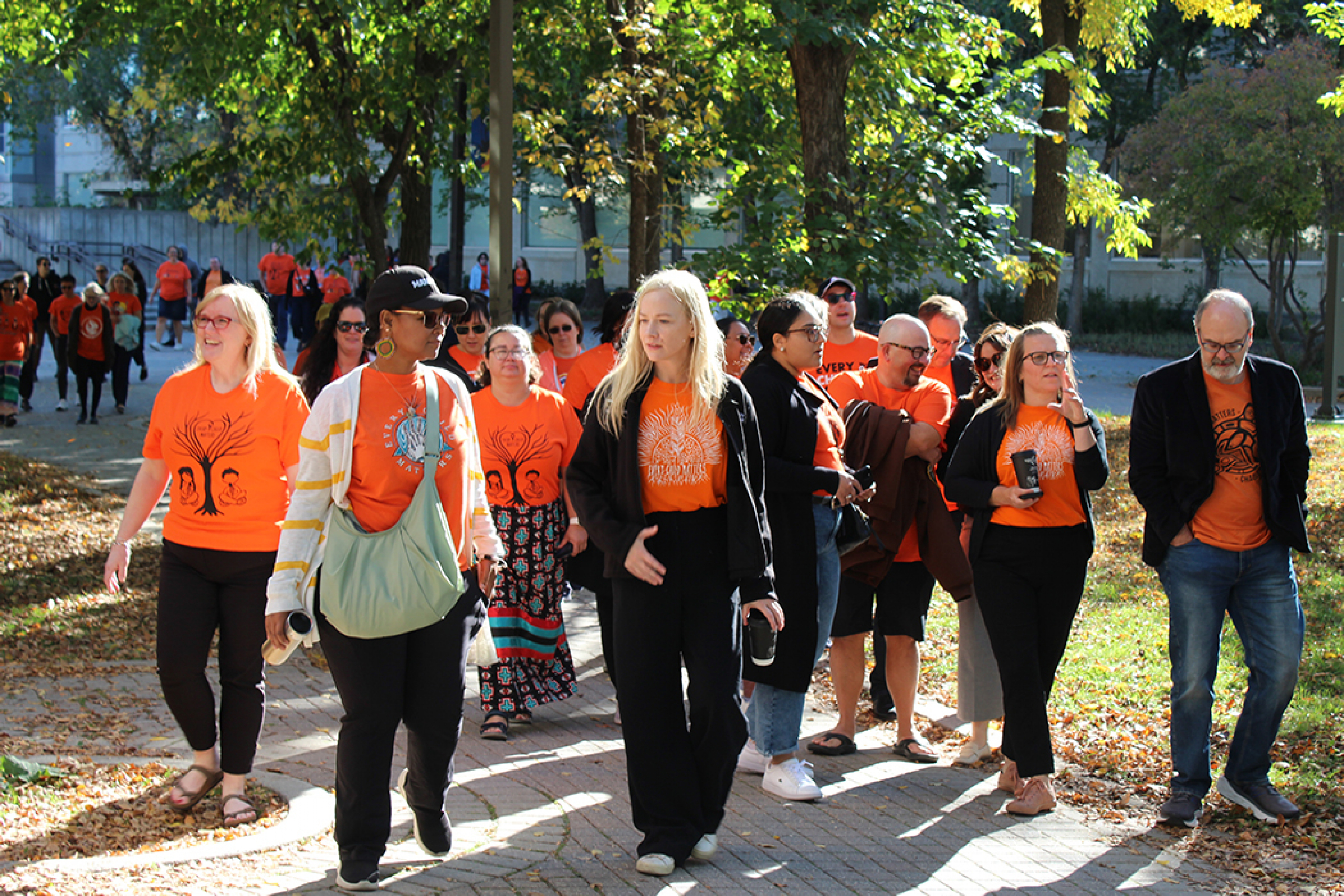 A group of people wearing orange shirts walk through Fort Garry campus, near the Helen Glass Centre for Nurisng.