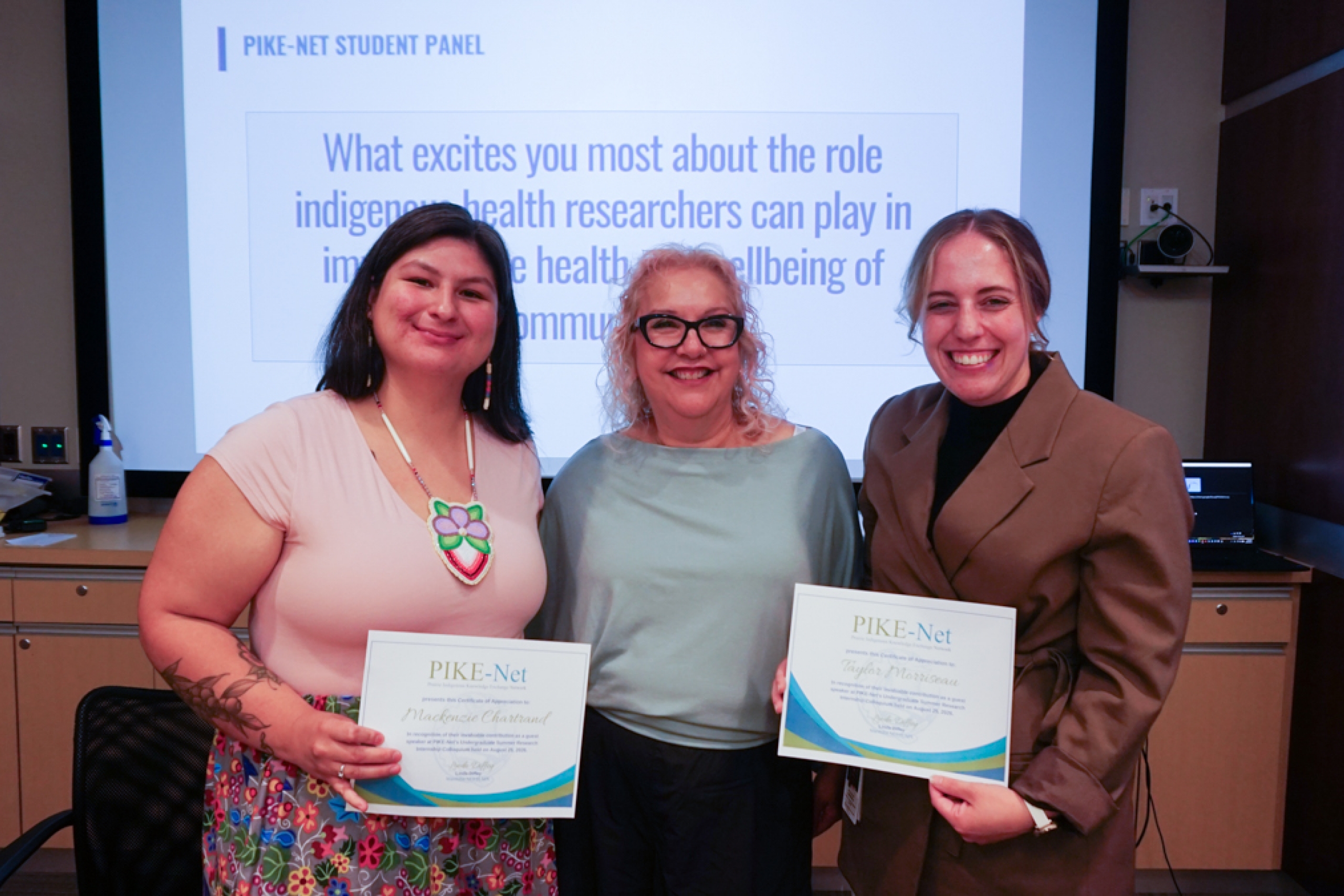 Three people pose for the camera, two of them each holding a certificate.