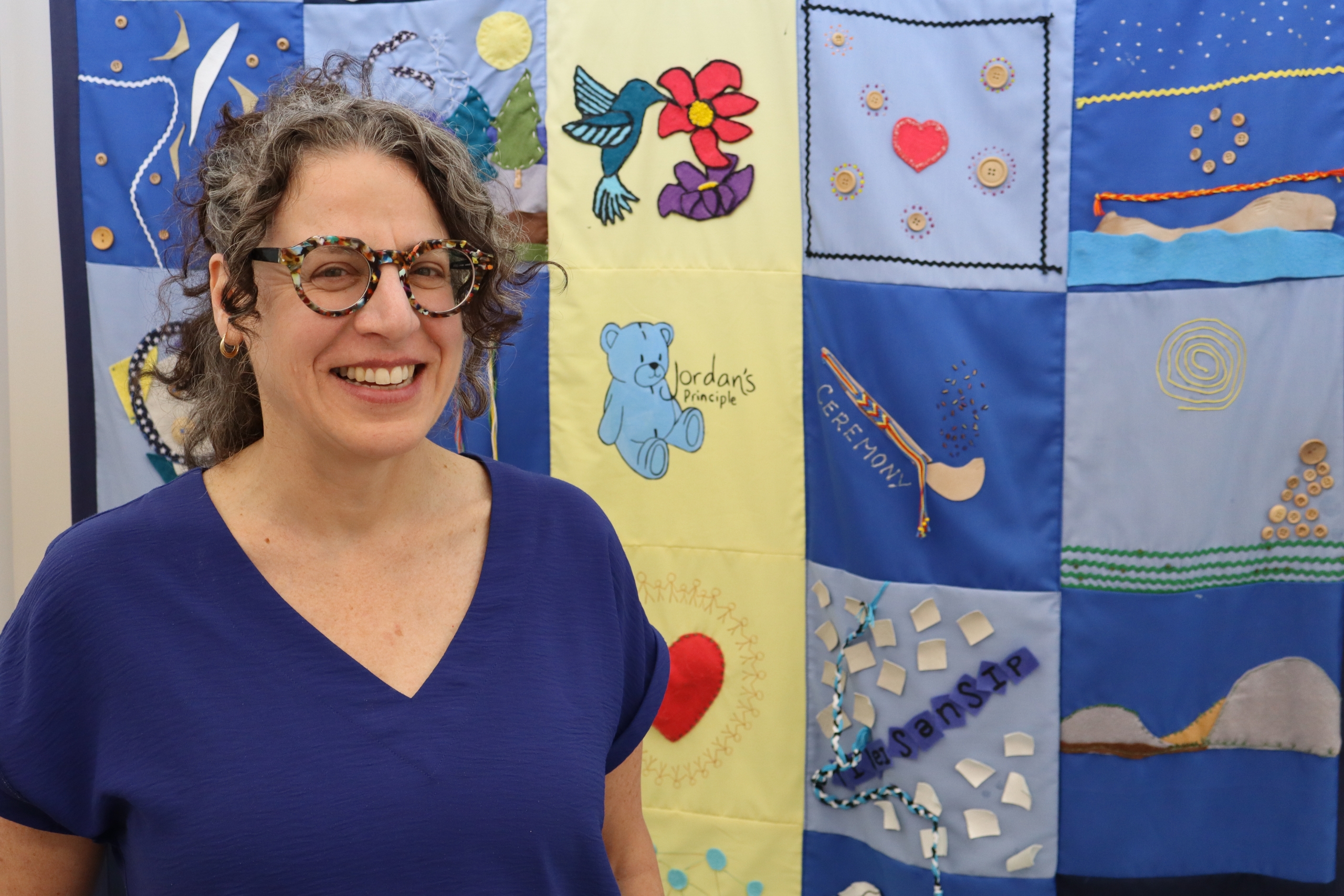 Pam Becker stands next to a quilt that features a Jordan's Principle logo.