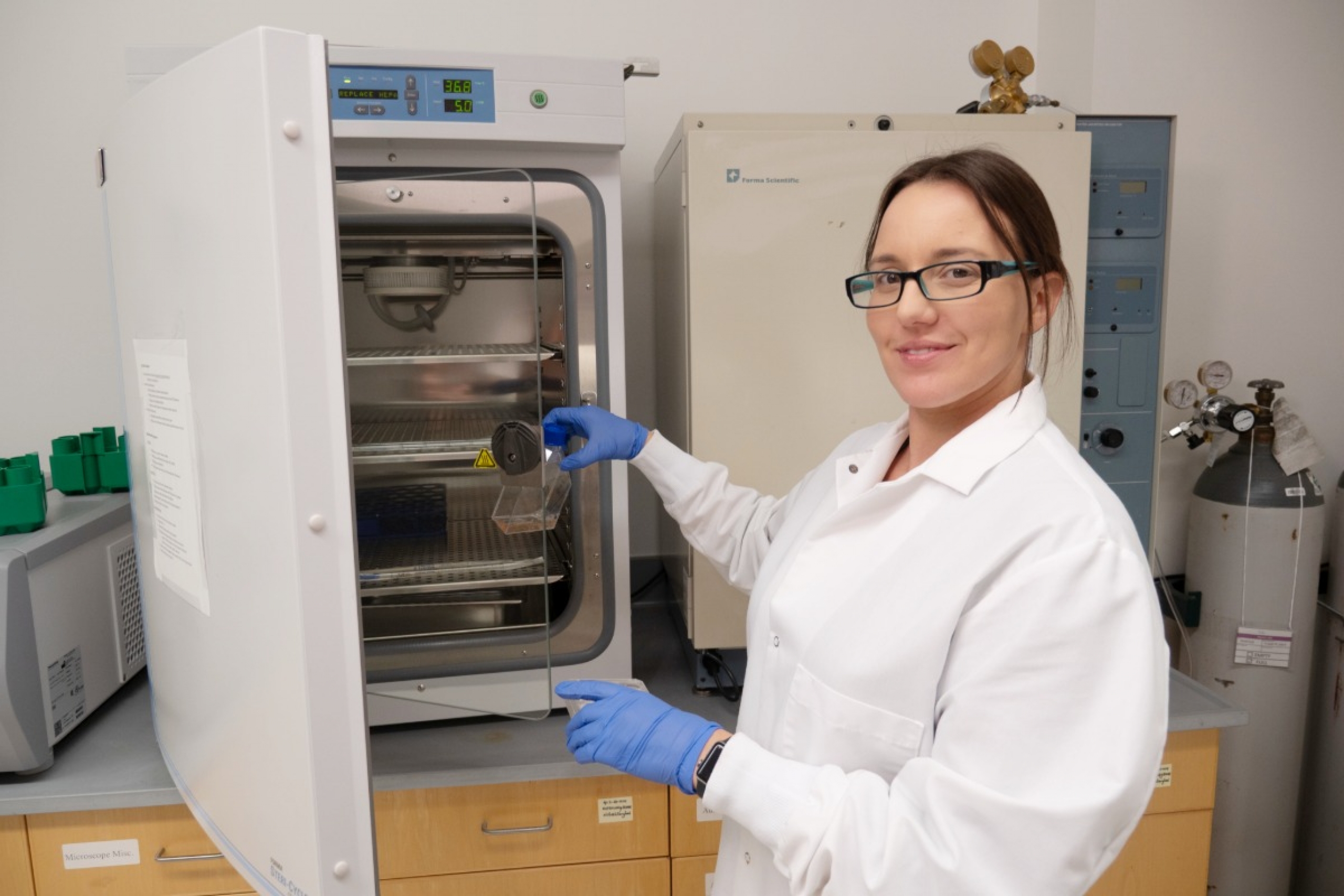 Scientist in a lab beside a fridge for specimens.
