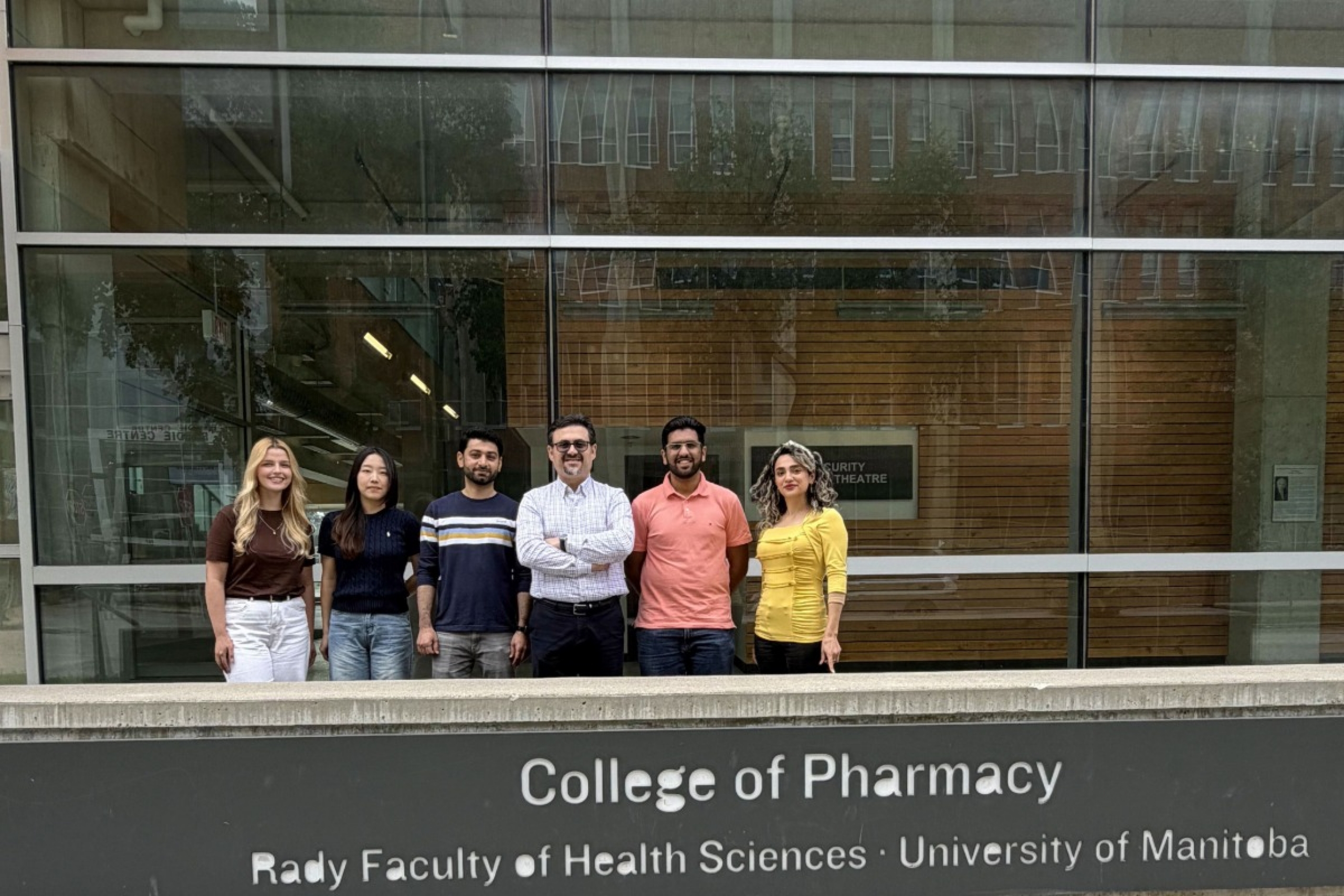 Six people stand behind the College of Pharmacy sign.