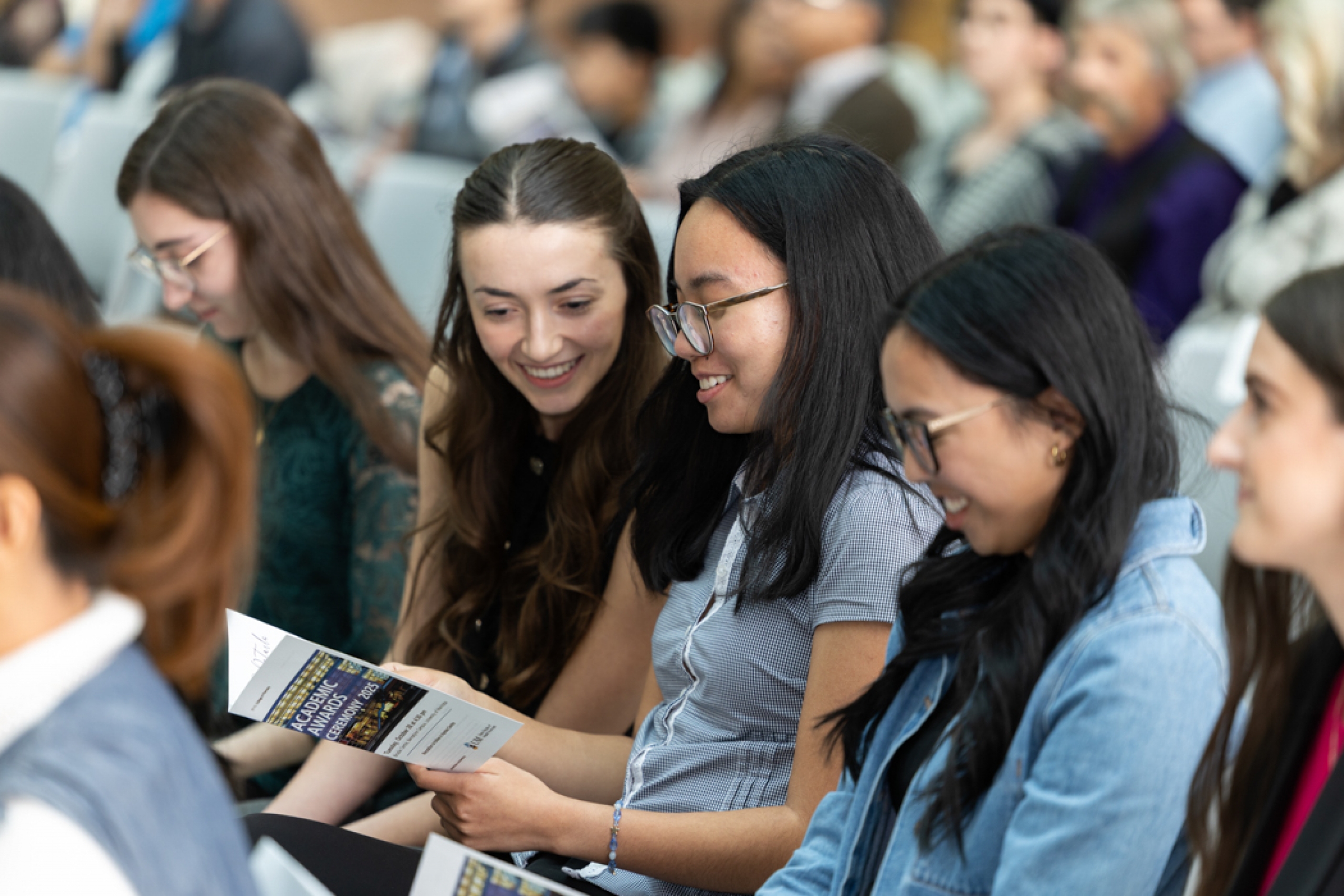 Students sit together, smiling and reading the event program.