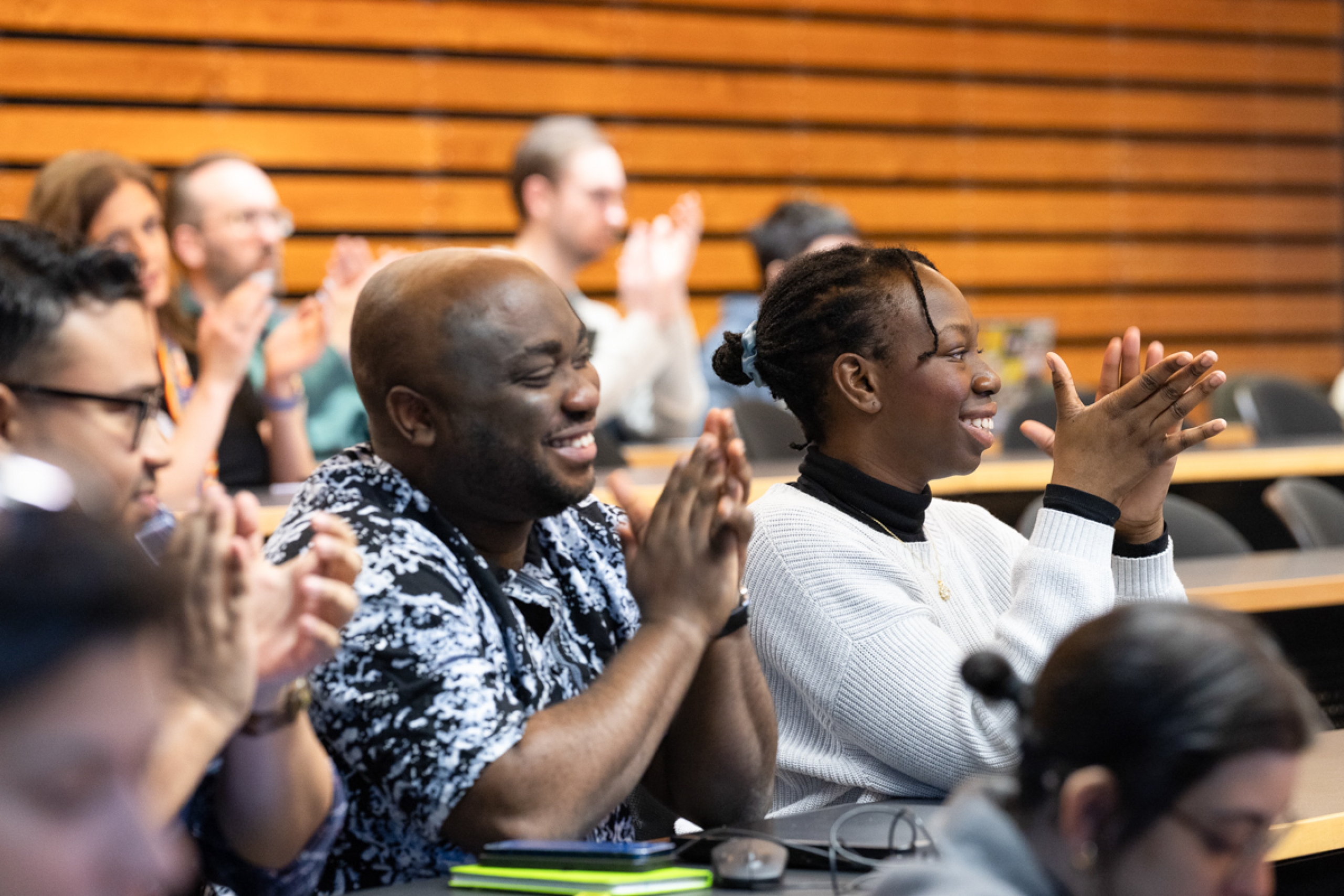 A crowd in an amphitheatre-style classroom clap and cheer.