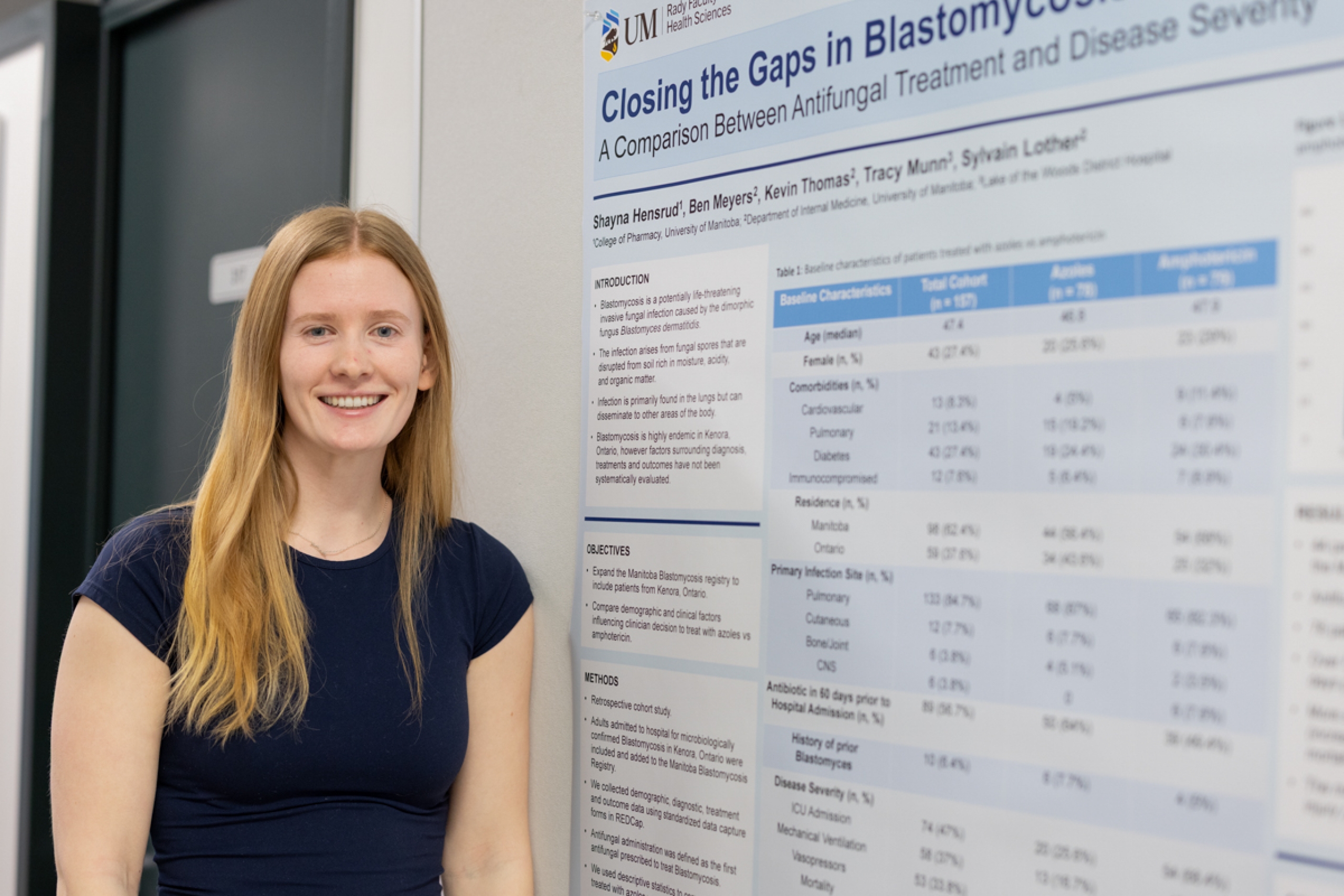 A student standing by their research poster smiles at the camera.