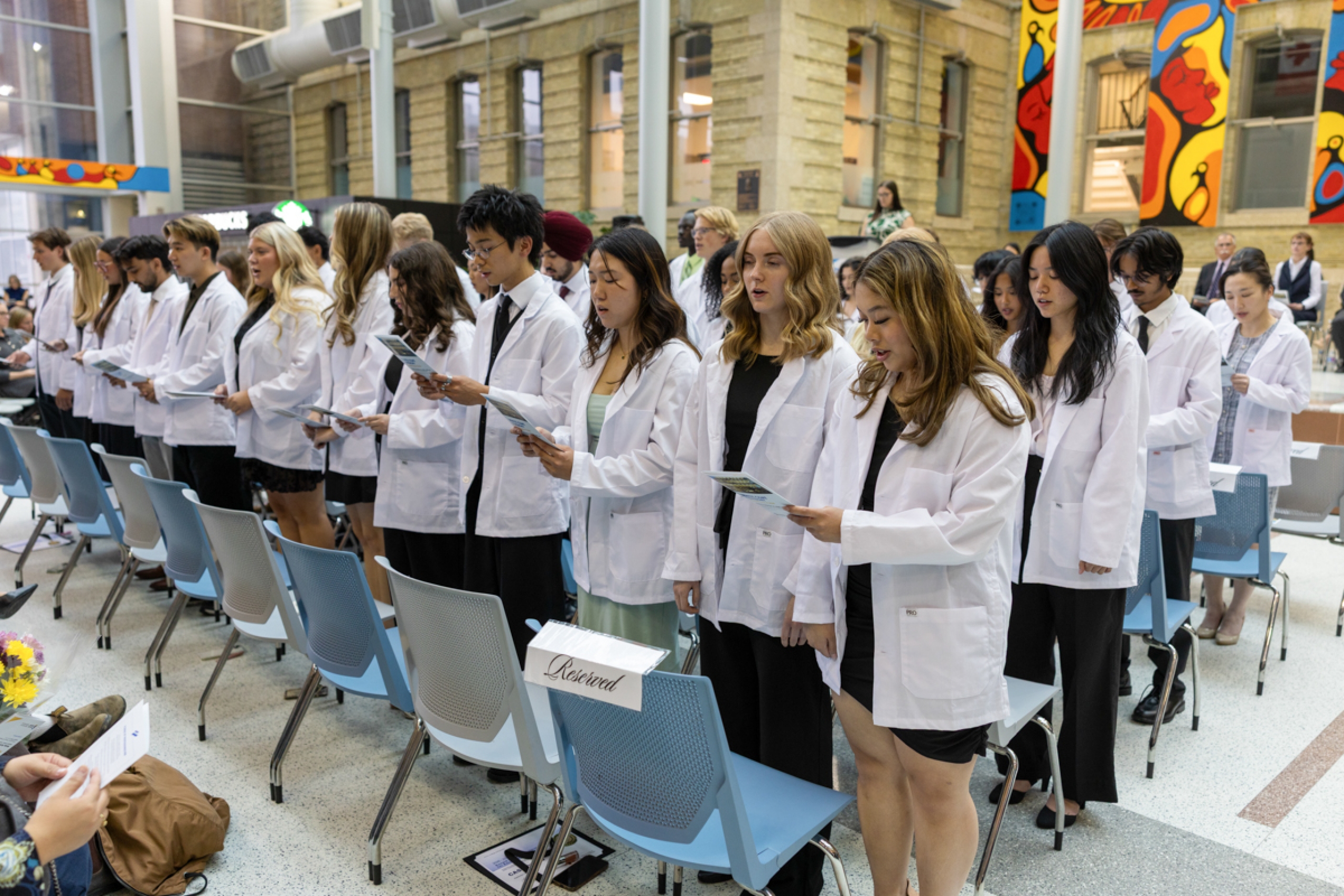 A group of students wearing white coats reciting a pledge.