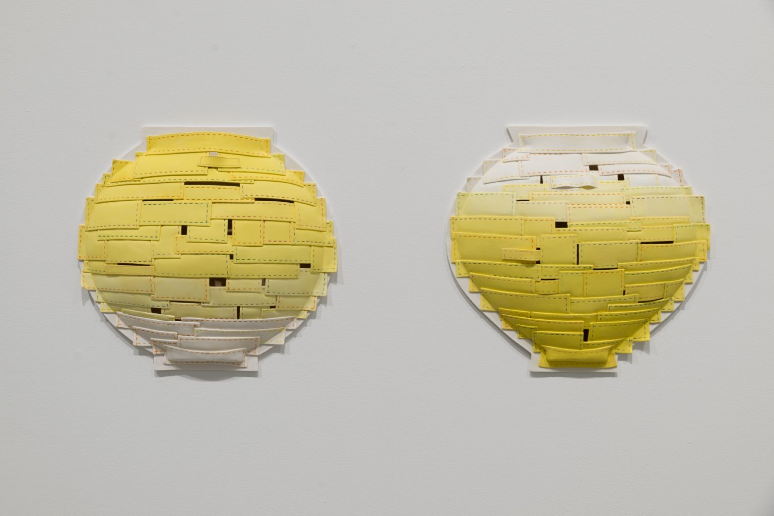Two yellow ceramic wall sculptures each forming basket-like geometric shapes on a white wall.