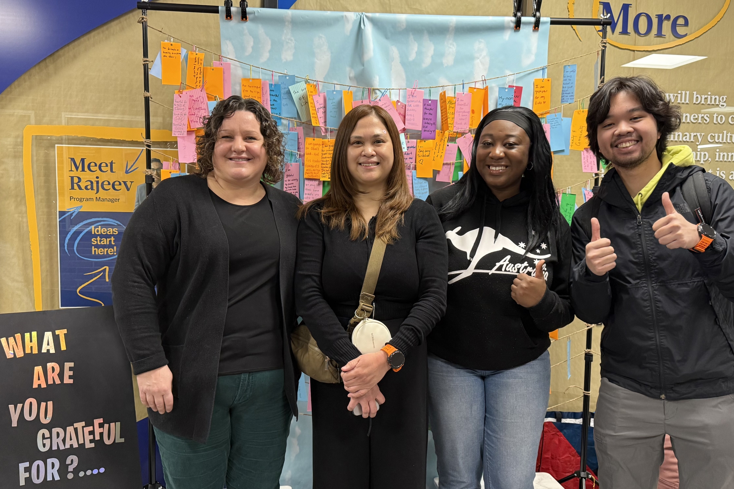 Four people at an event in a line posing for the camera in front of a hanger full of ideas.