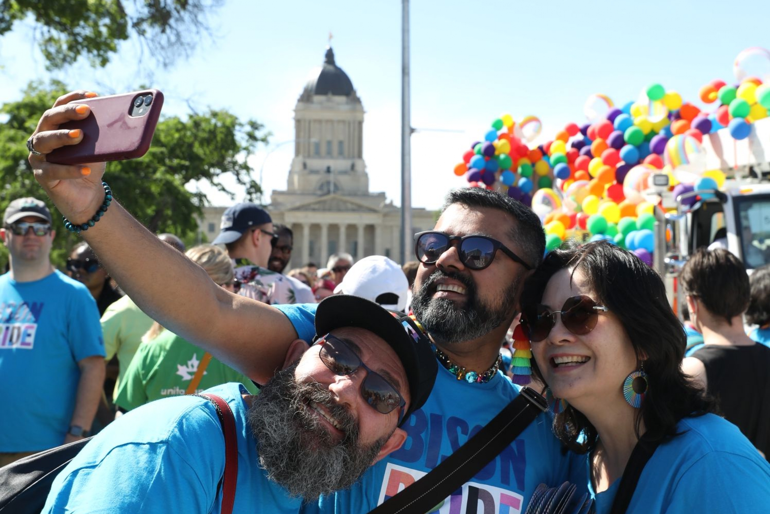 Three people pose for a photo at the Winnipeg Pride Parade.