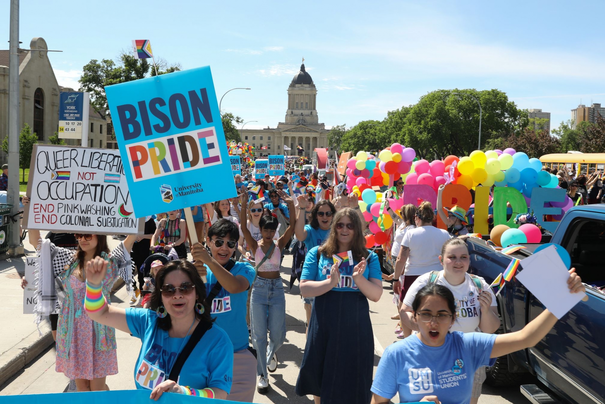 UM community members walking in Pride Winnipeg Parade, carrying banners and signs.