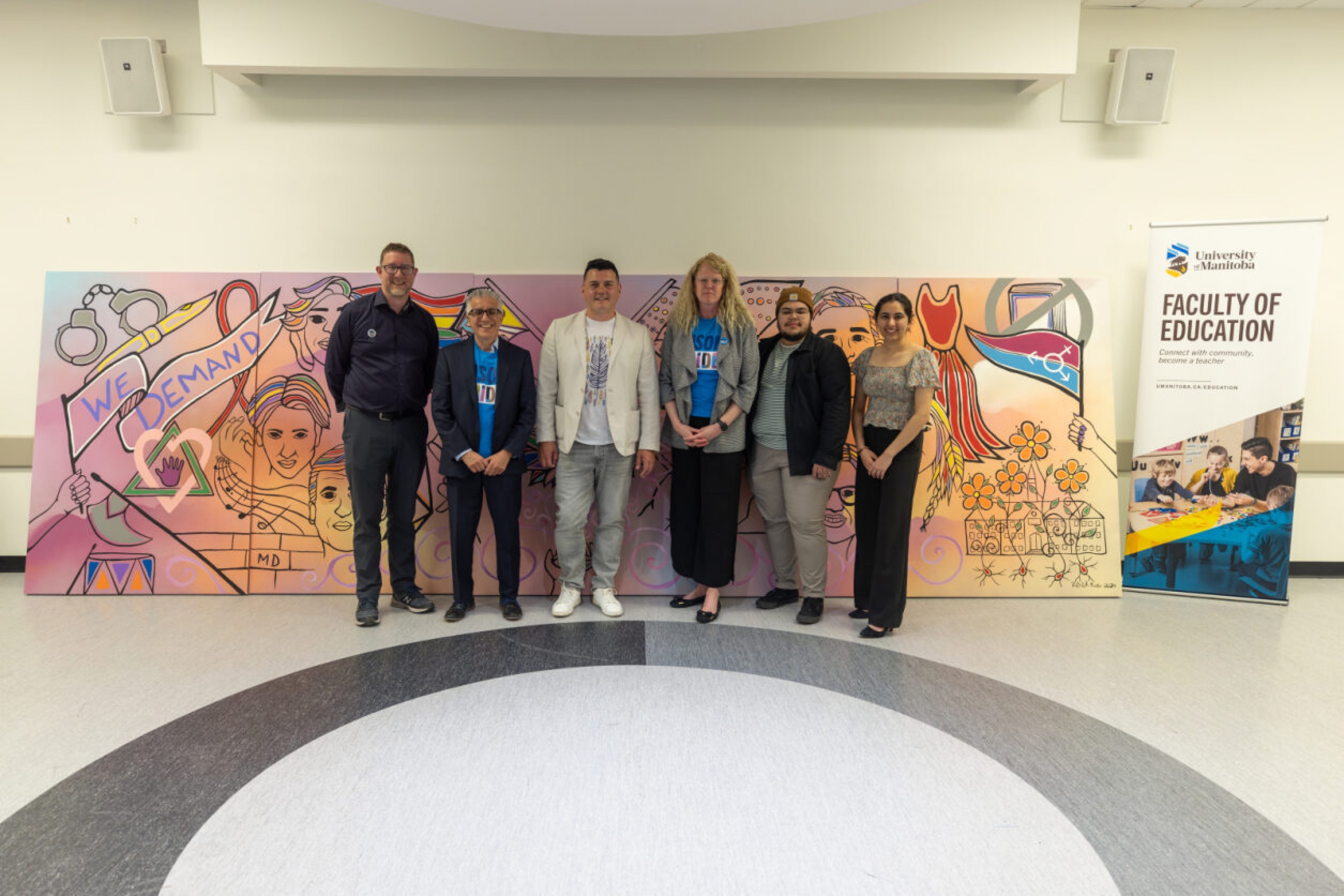 Six people including artist Patrick Hunter and Michael Benarroch pose in front of Hunter’s Mural.