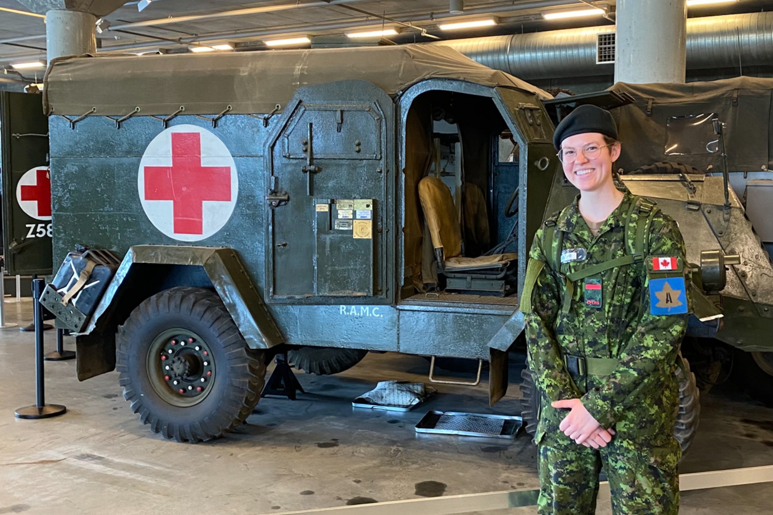 A person in military uniform in front of an armoured ambulance in a museum.