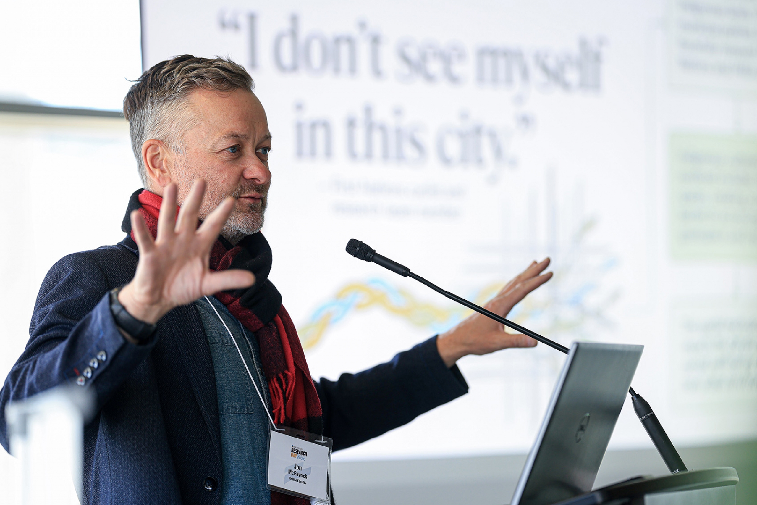A man stands at a podium talking with his arms. The screen the presentation says I don't see myself in this environment.