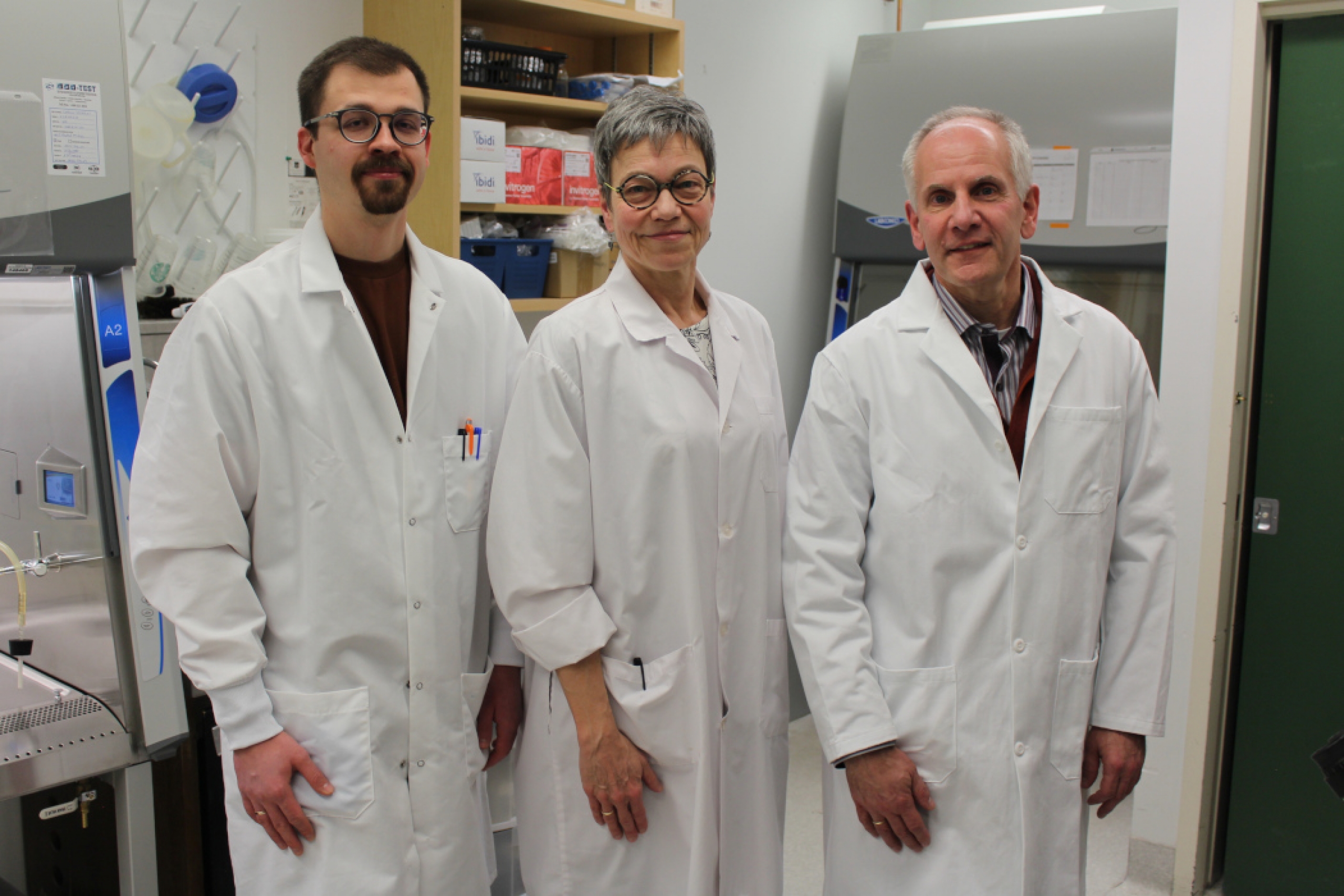 Three people wearing lab coats pose for photo in a lab. 