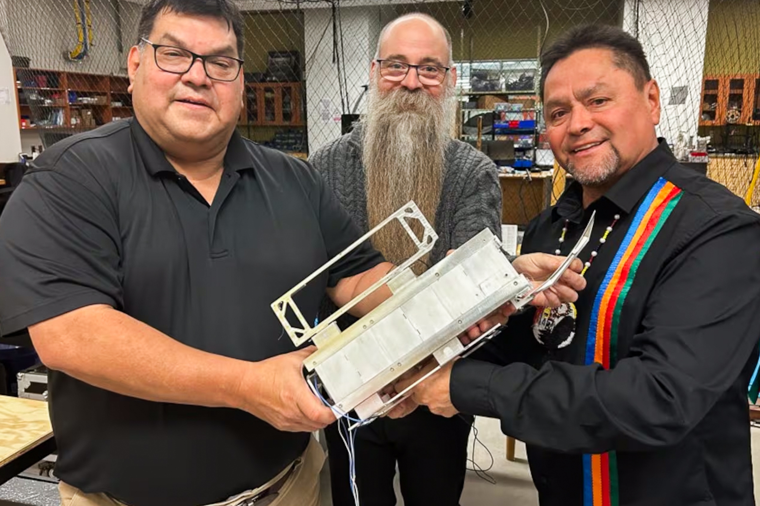 Three men pose with a mechanical device