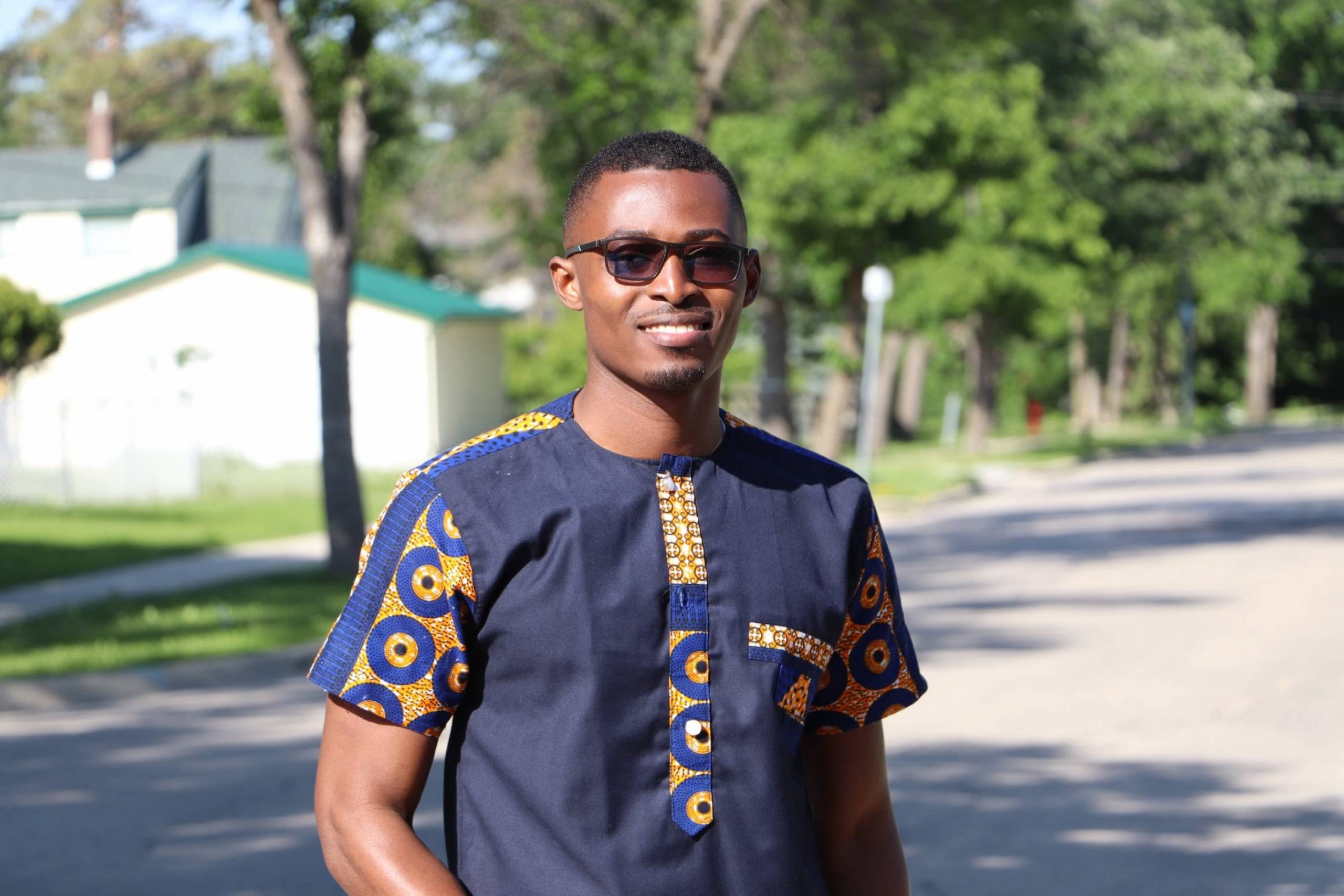 Young Black man outdoors with green trees in background.