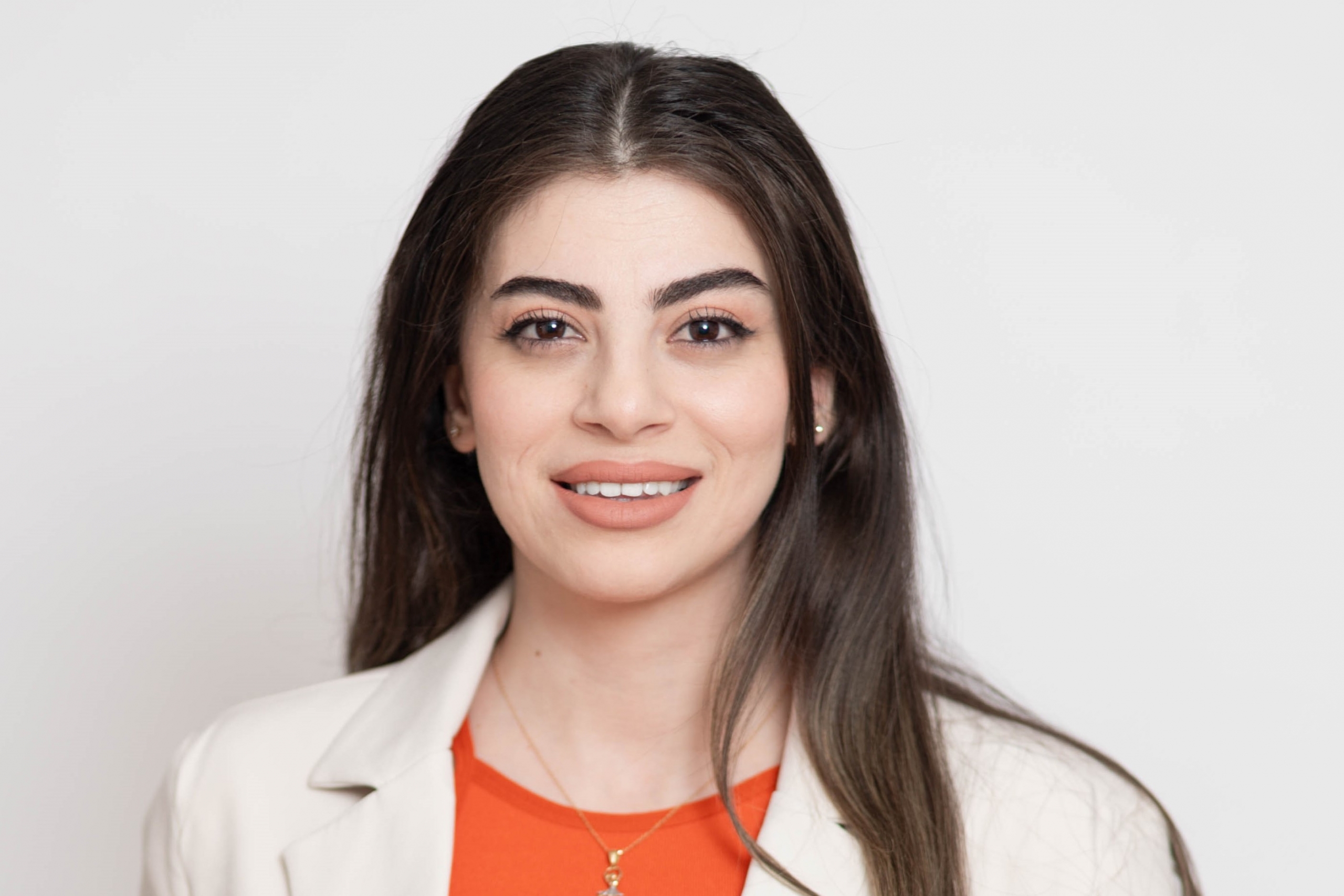 Professional portrait of a smiling woman with long dark hair, wearing a beige blazer over an orange top.