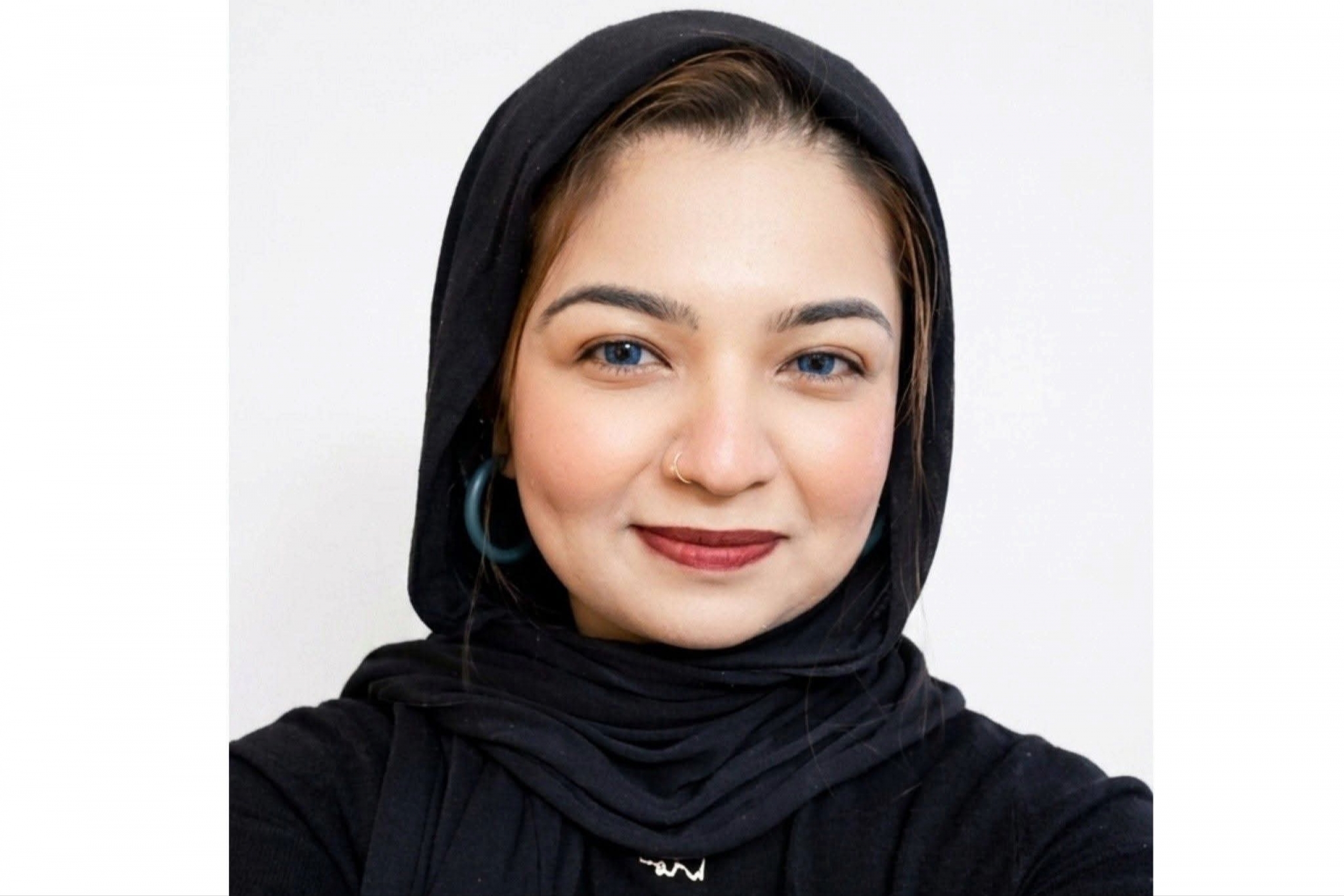 a woman in a black headscarf, gold necklace and round blue earring smiles brightly