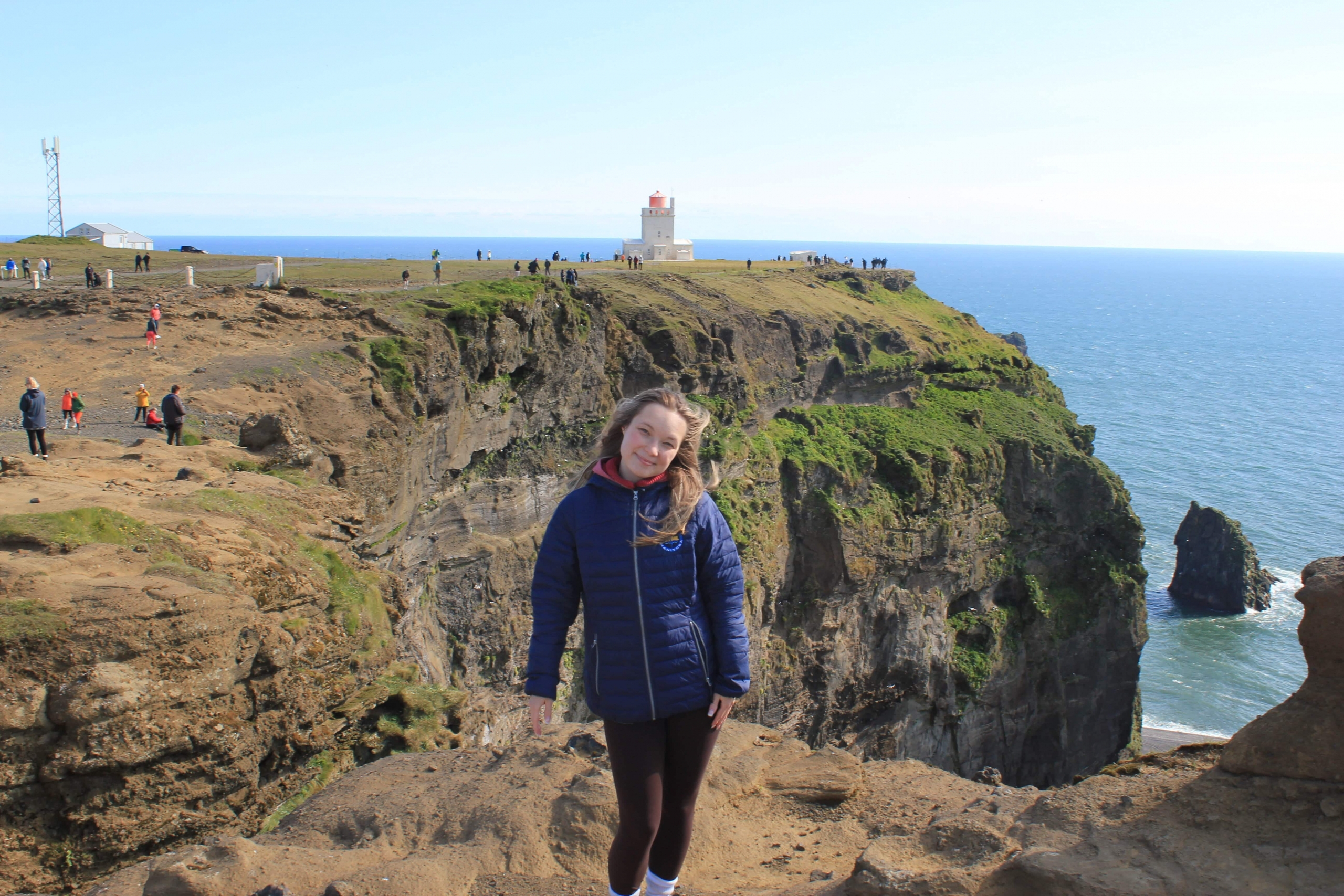 A female standing outside in front of a seaside cliff. 