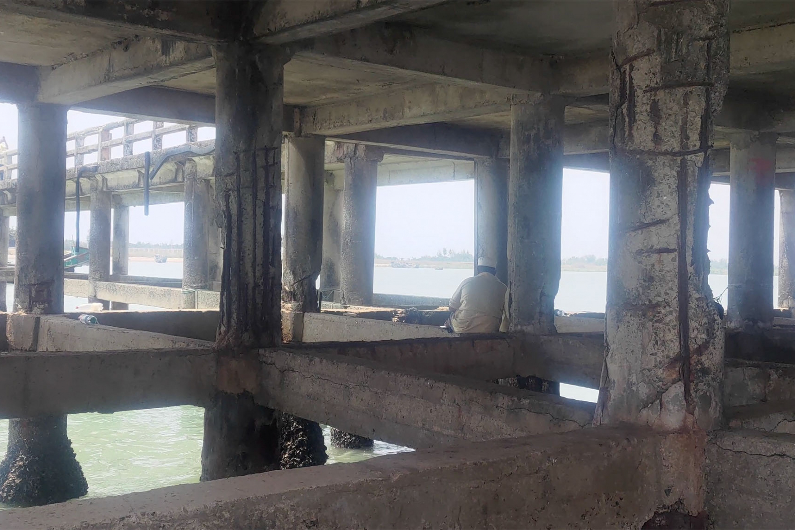 The underside of a concrete pier where fishermen sit fishing with rods.