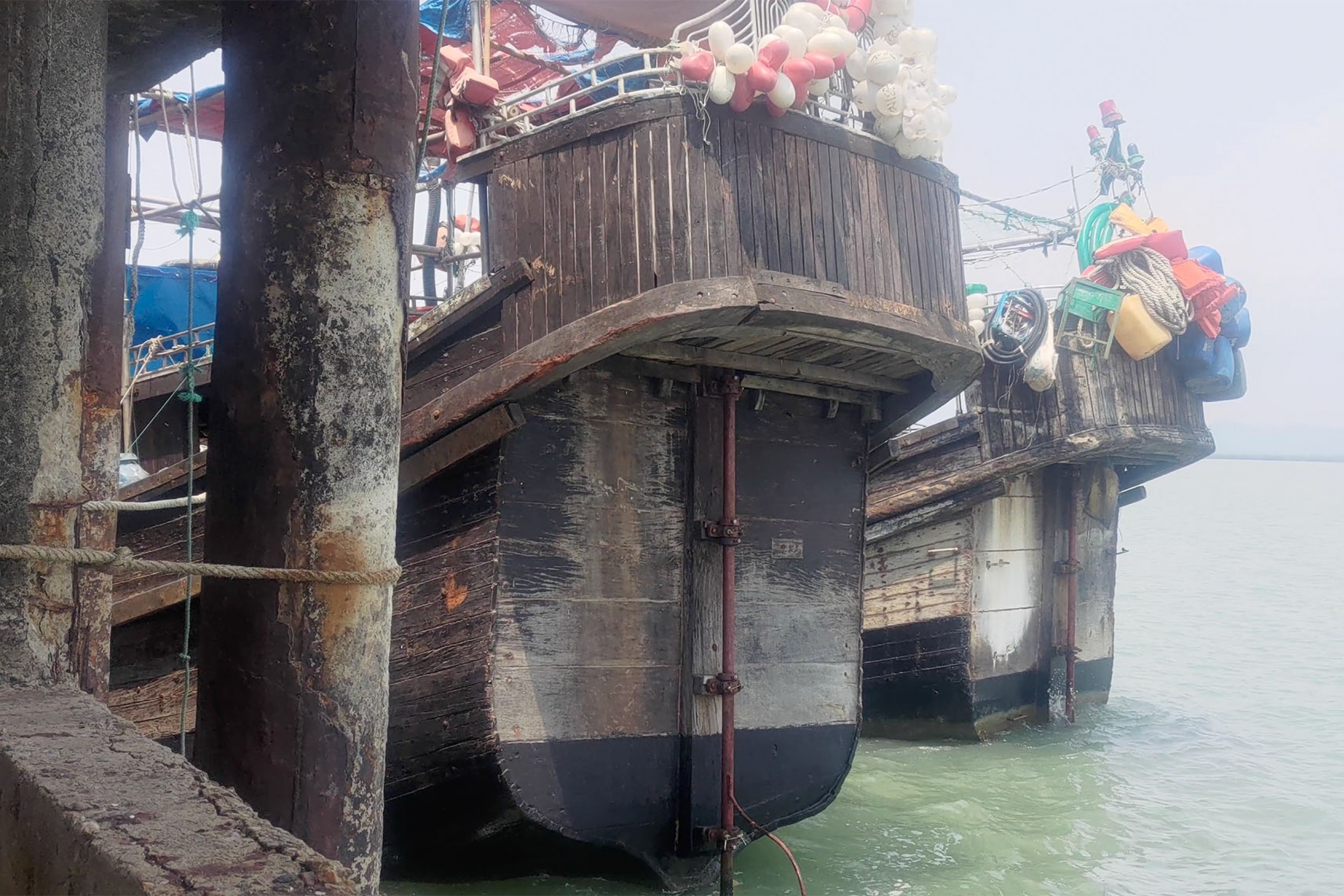 large old wooden fishing boats float on green water next to concrete pier posts