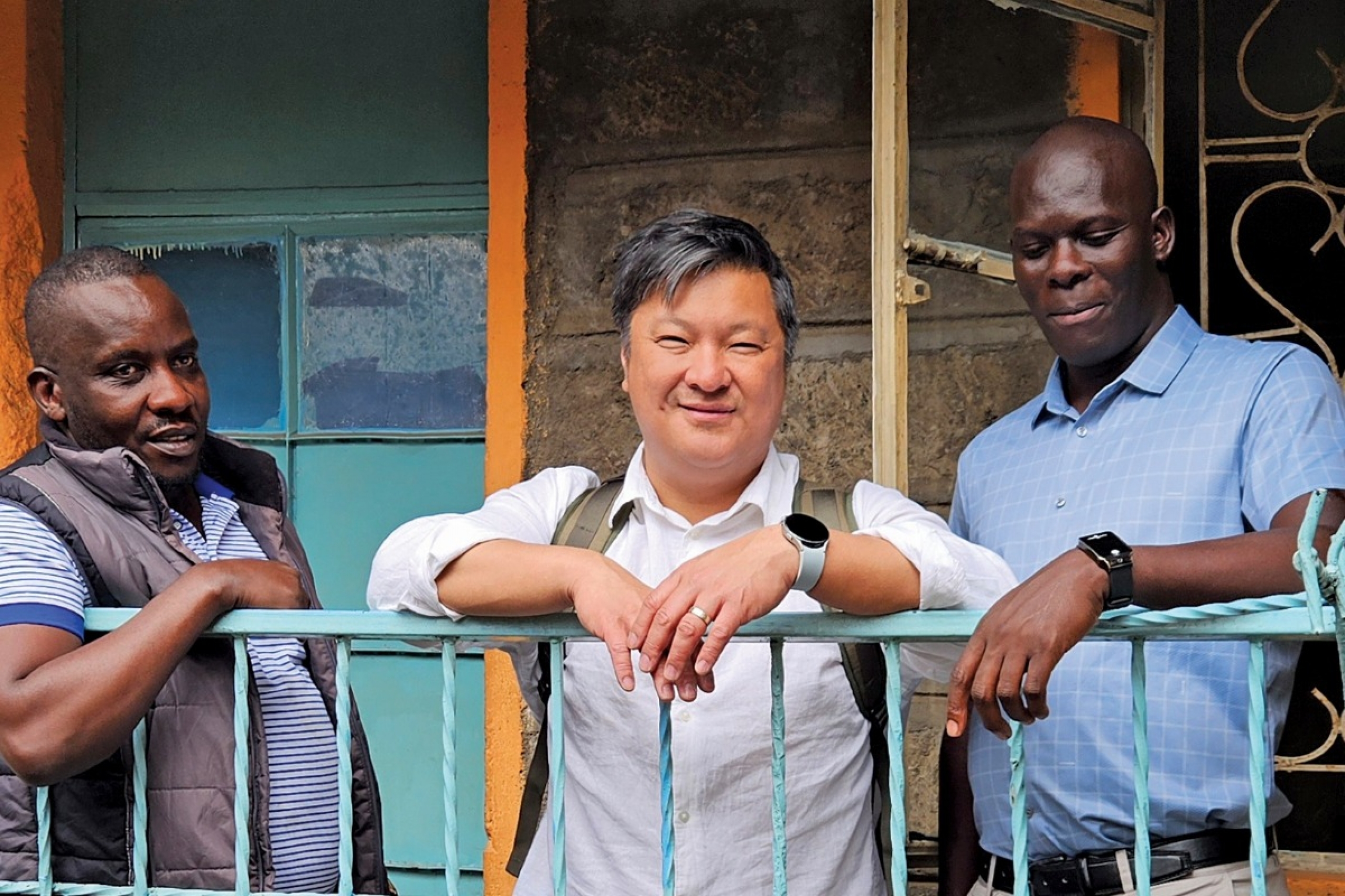 Dr. Souradet Shaw stands with two research collaborators outside a building. They lean on a fence.