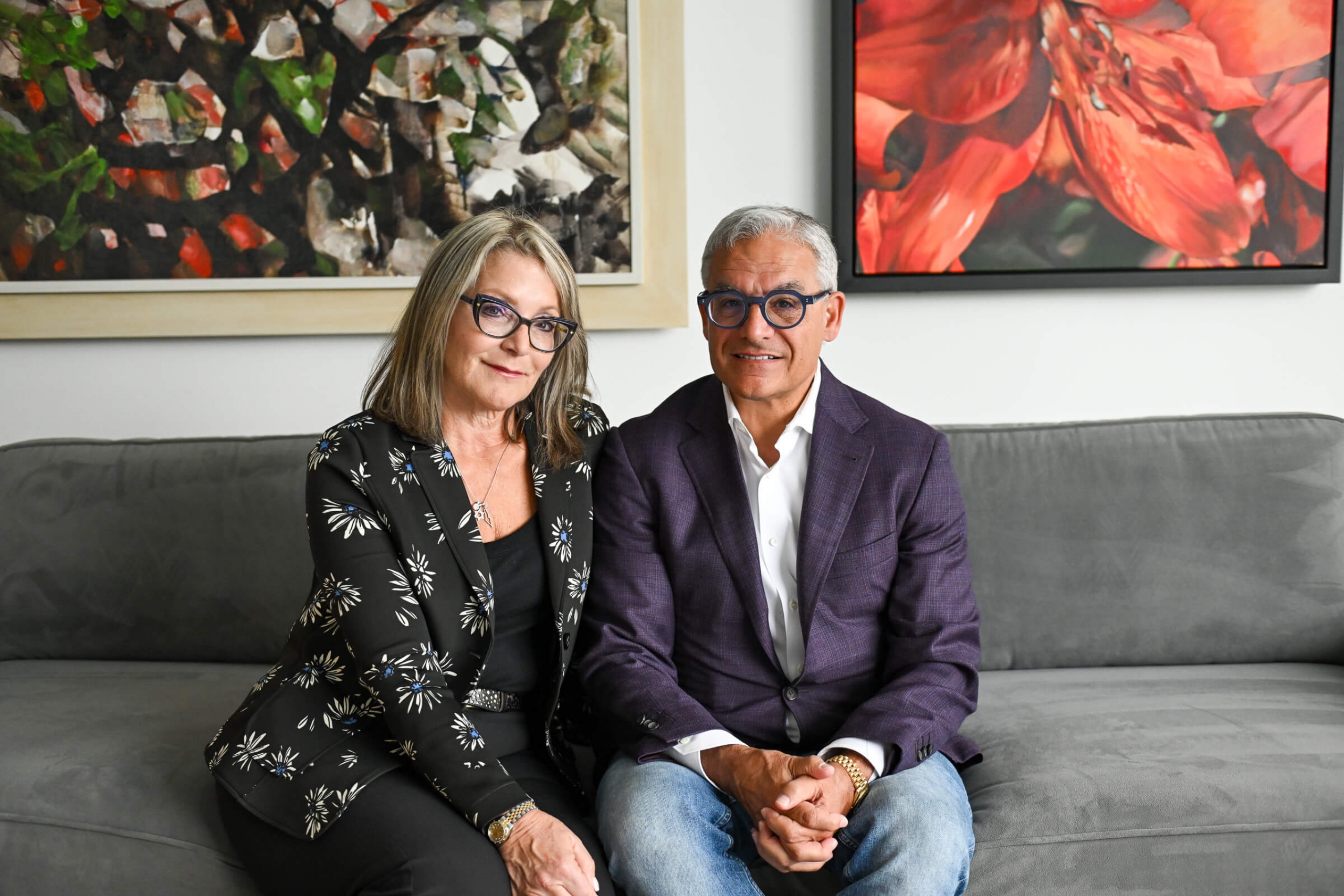 A man and woman sit next to each other on the couch looking at the camera