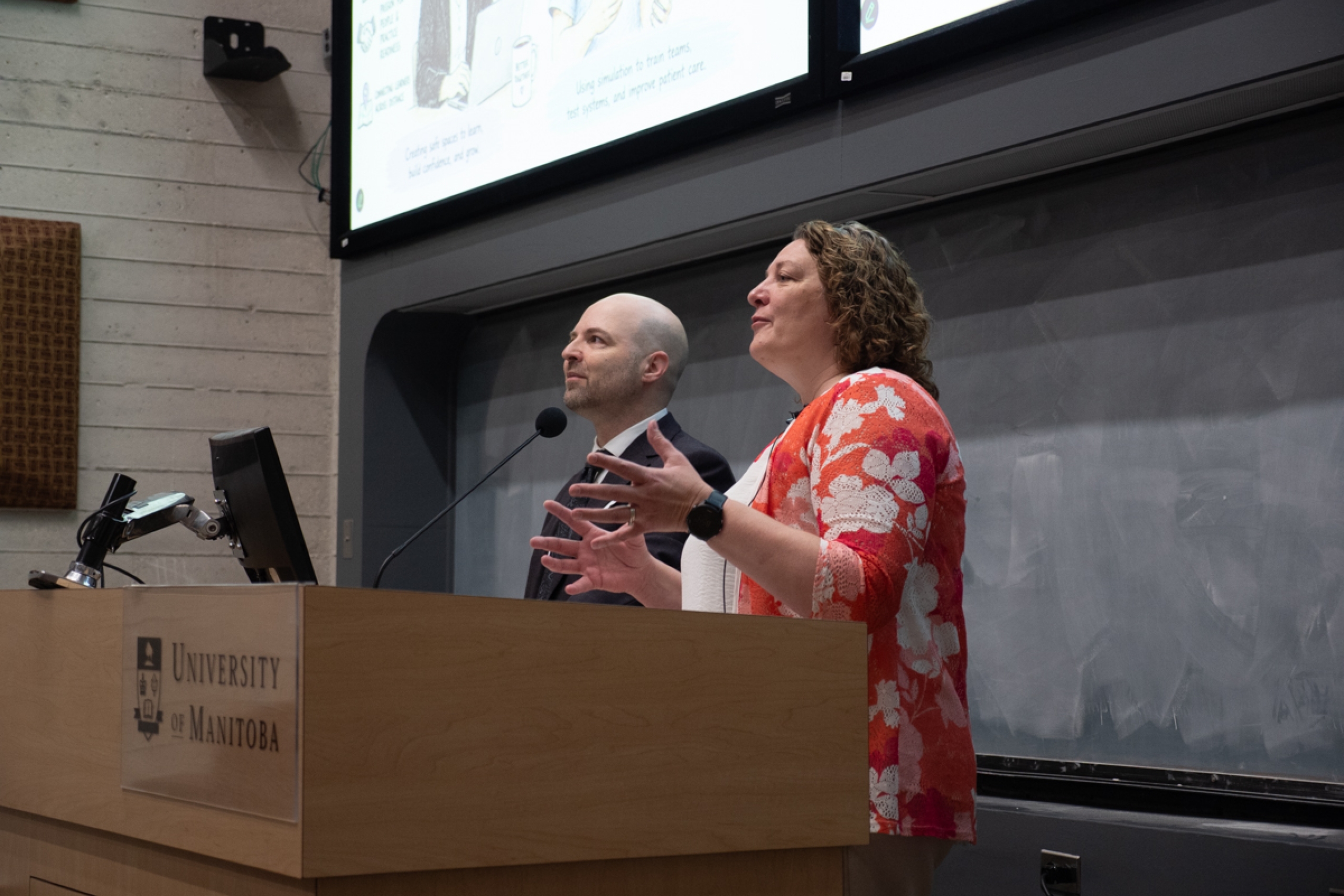 Two people speak in front of a podium.