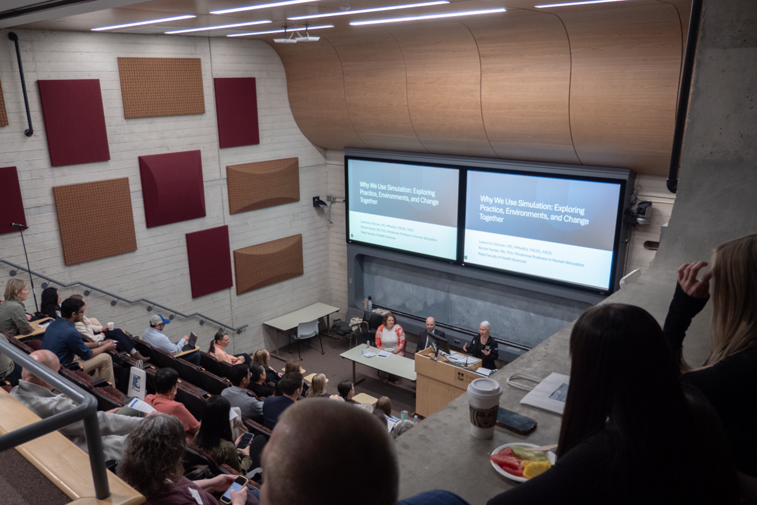 A theatre style classroom with an audience and a person talking at the podium.