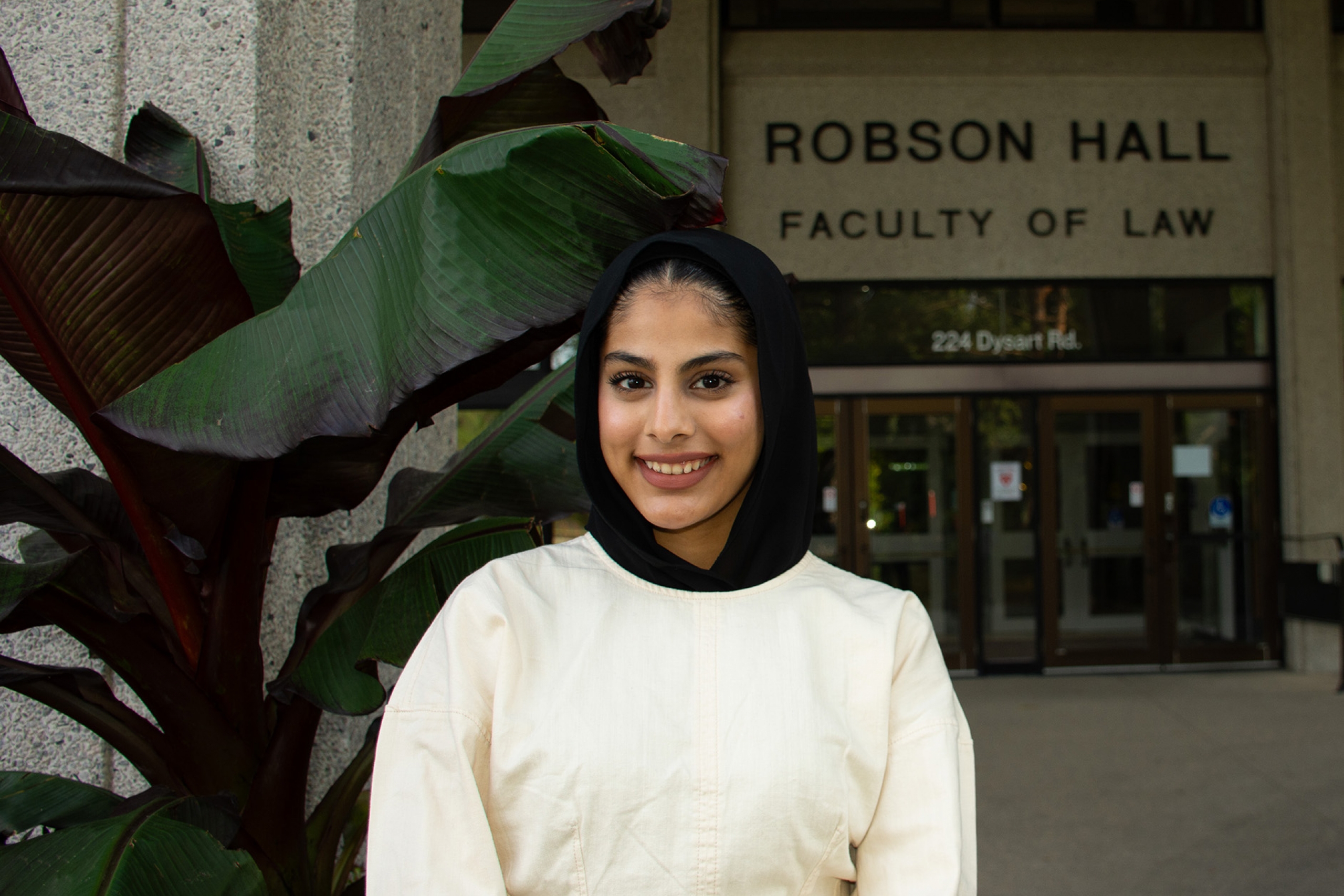 Internationally trained law student Sofia Shoukat stands in front of a large leafy plant in front of Robson Hall