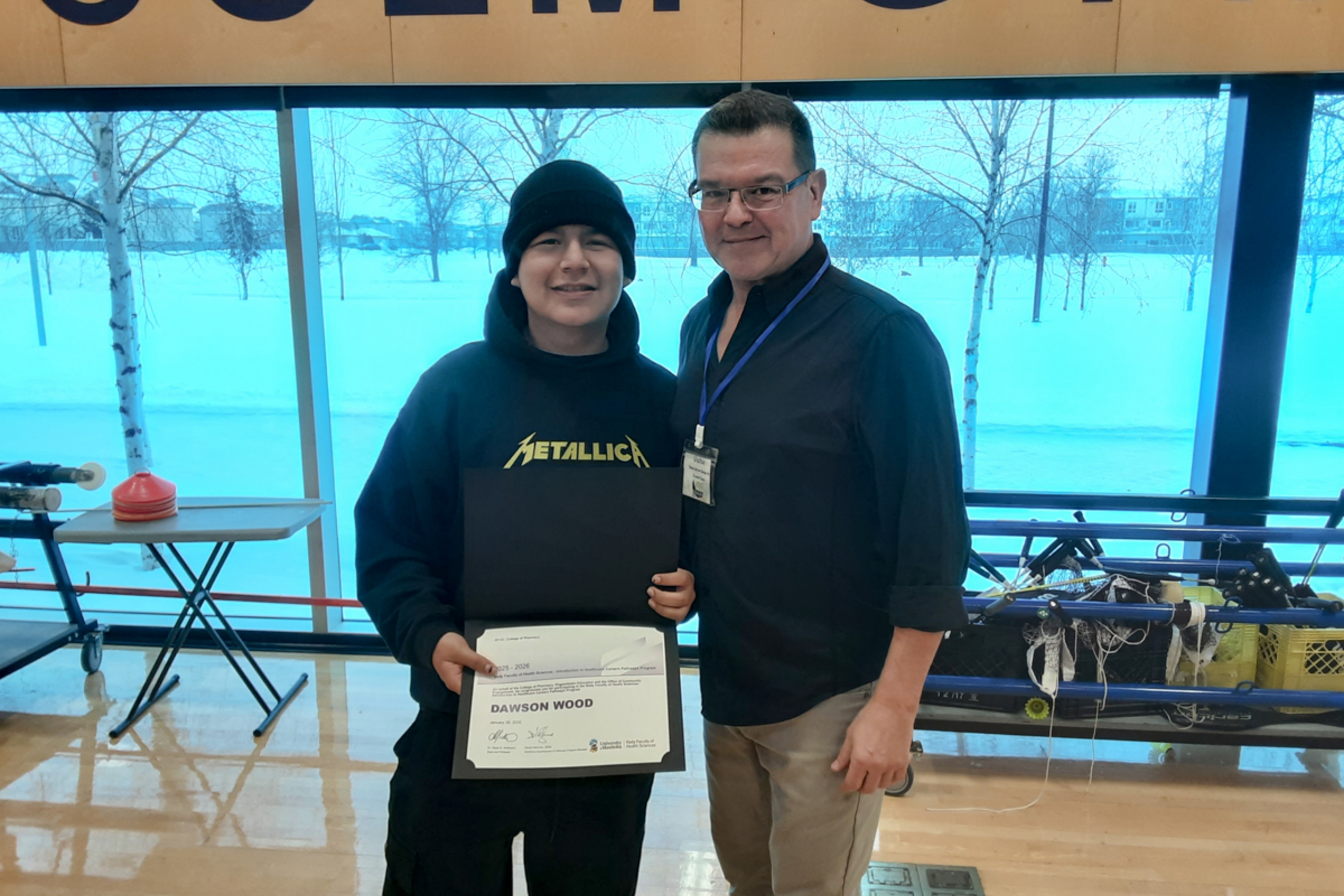 Two people smiling at the camera, person in the left holds a certificate.
