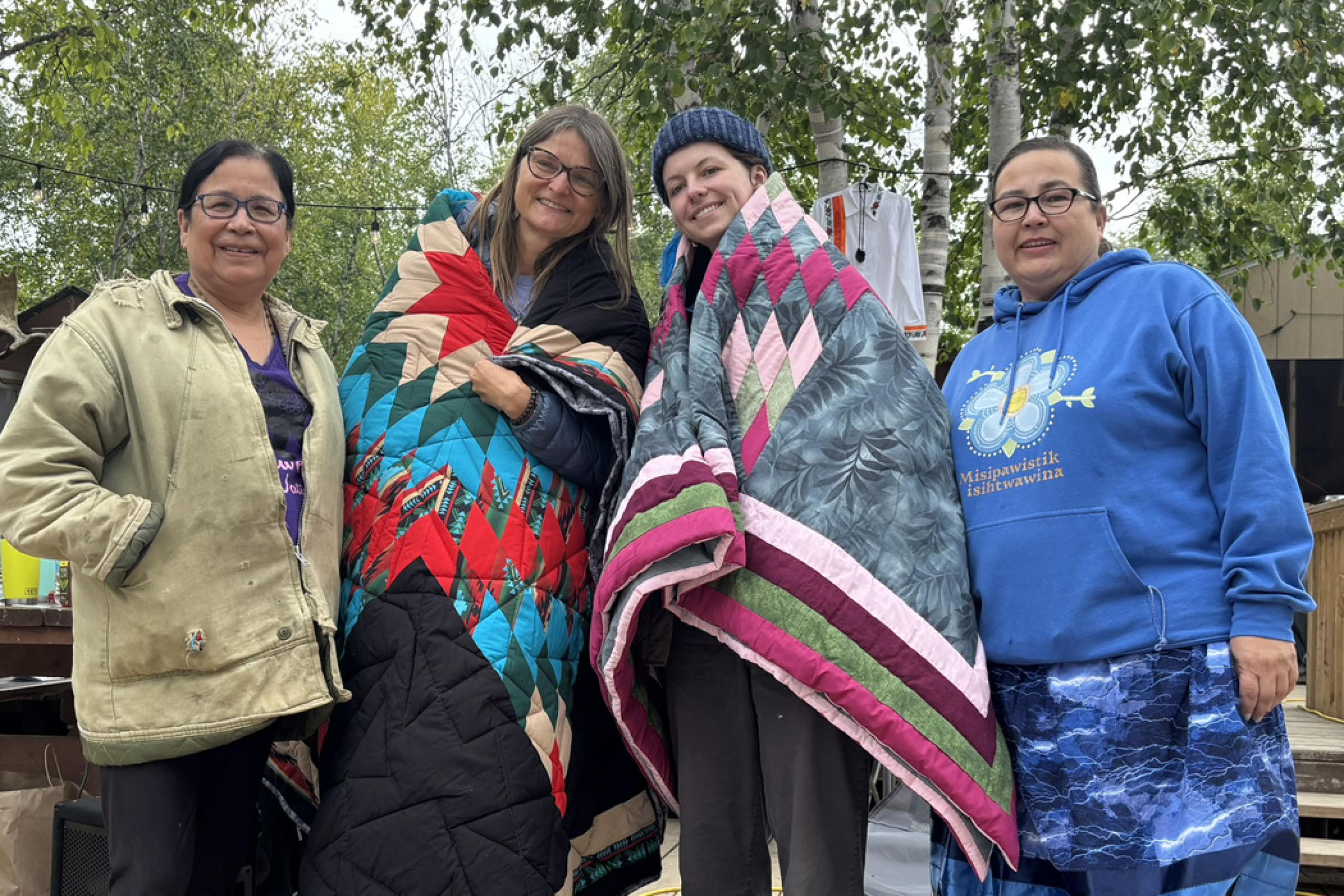 Lisa Mendez and Maura Macaulay wear star blankets and pose alongside Esther Cook and Margaret McGregor at Misipawistik Cree Nation.
