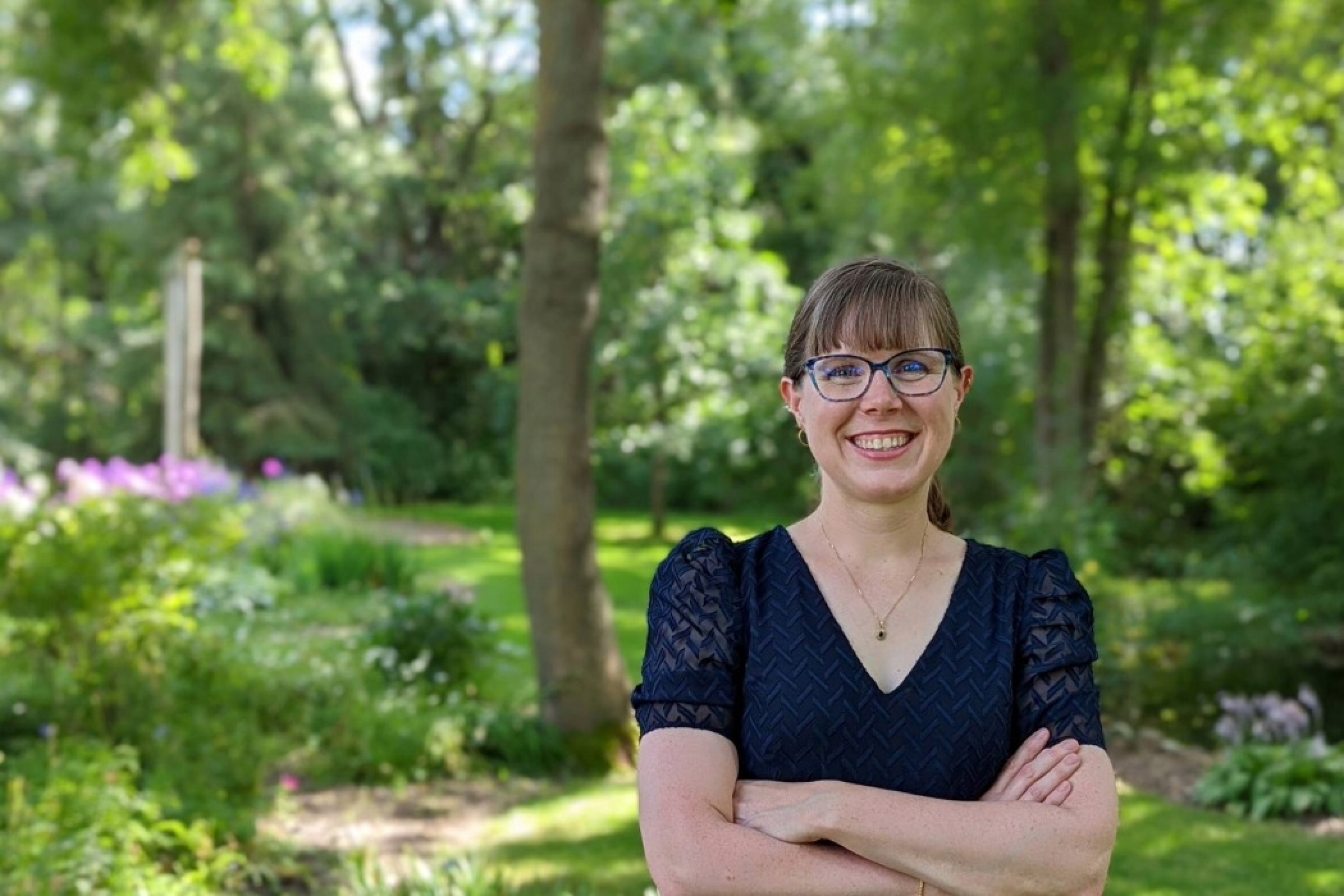 Jill Stobart smiling at the camera in an outdoor setting with trees and bushes.