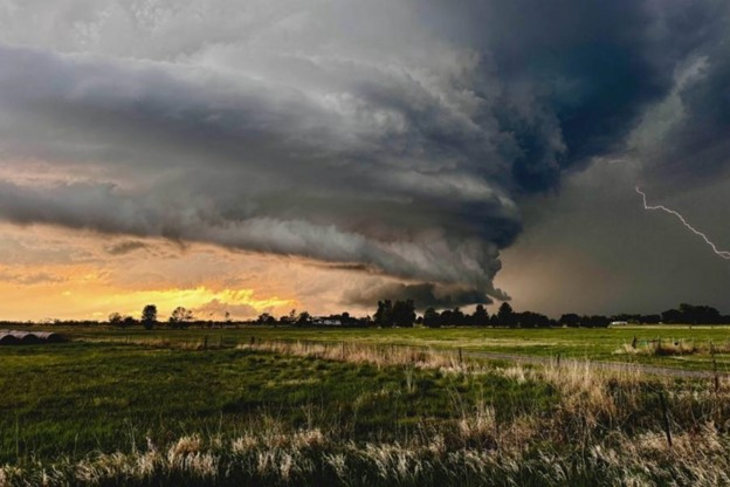 Dark, swirling clouds are forming an intense storm over a grassy field.
