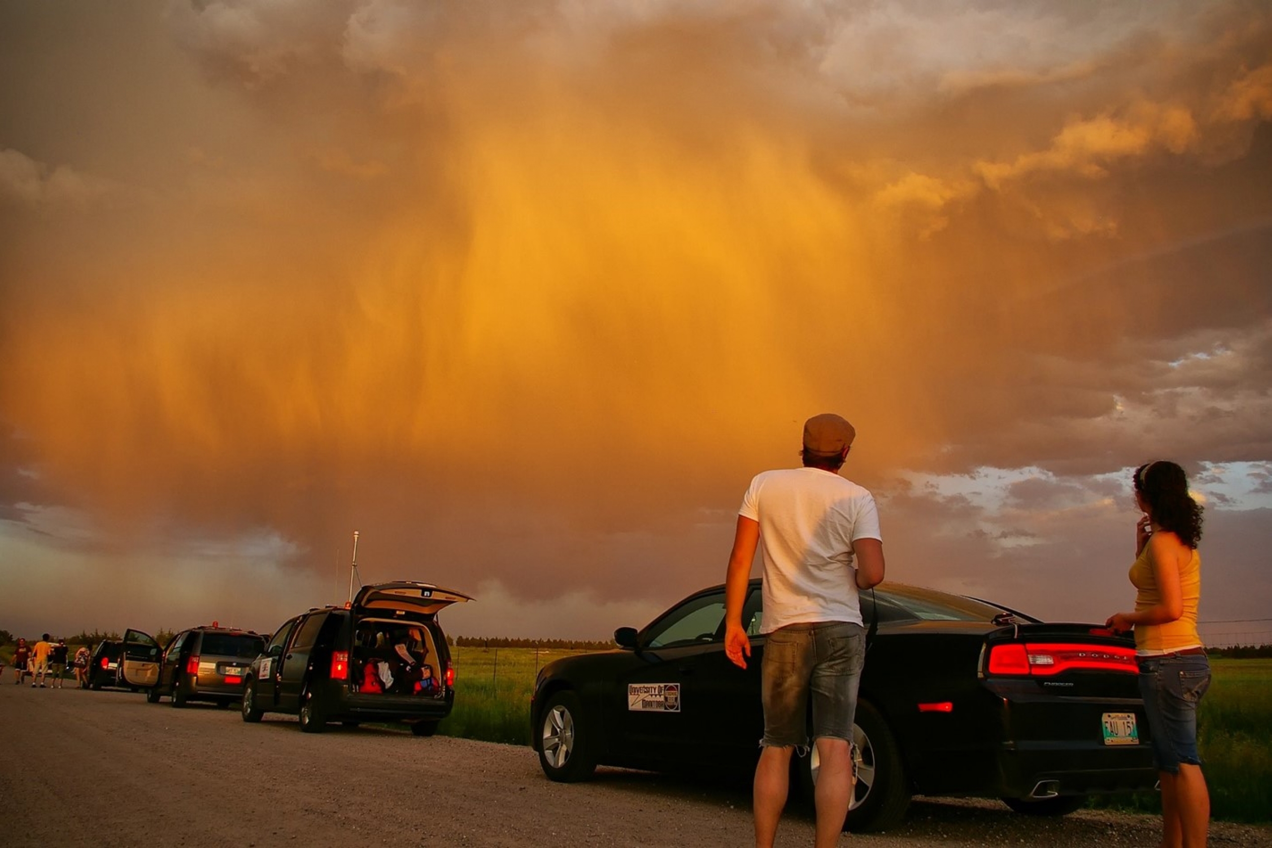 Vehicles are lined up on a road beneath clouds reflecting the sunset.