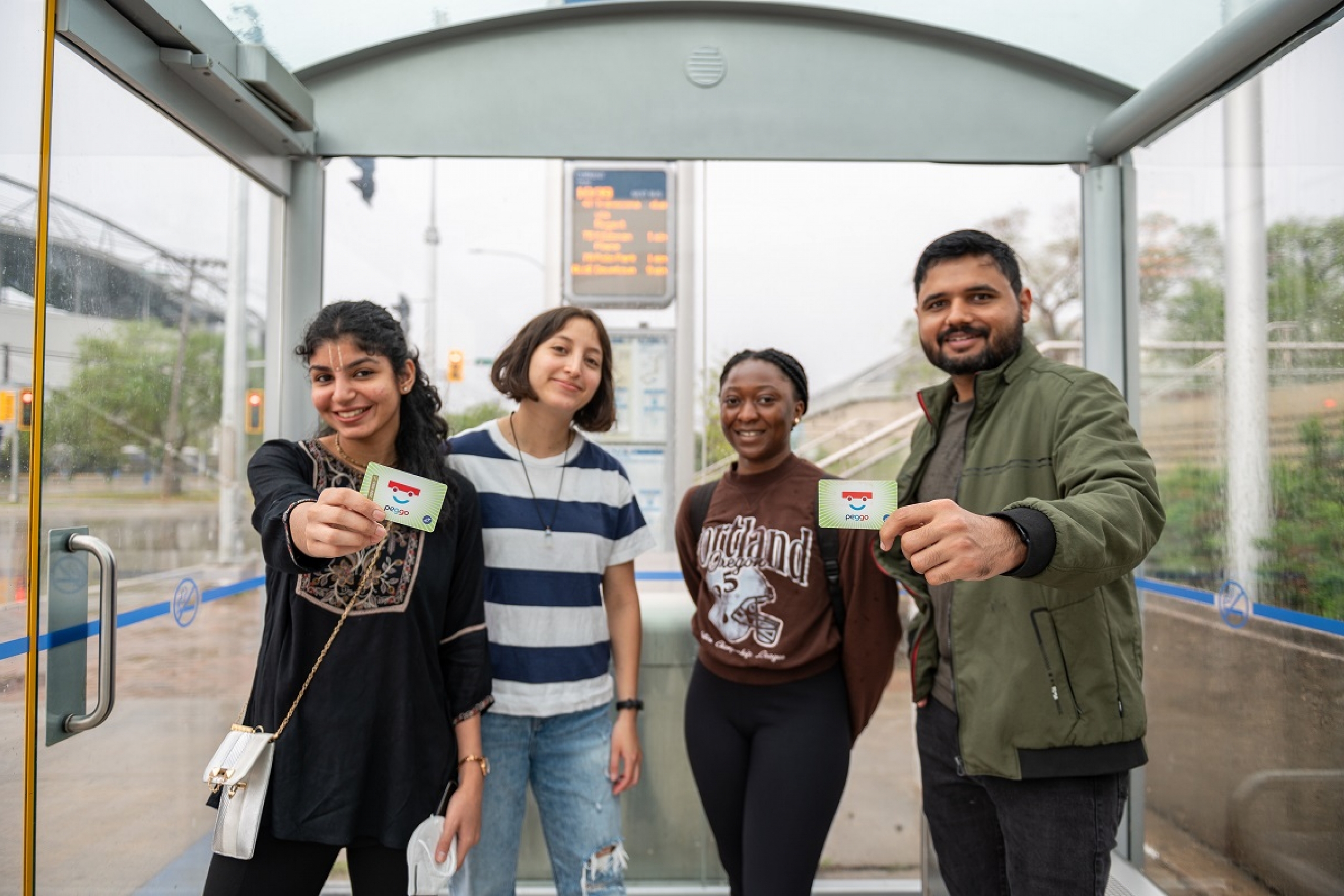 Four students stand together within a bus shelter while showing their U-Pass