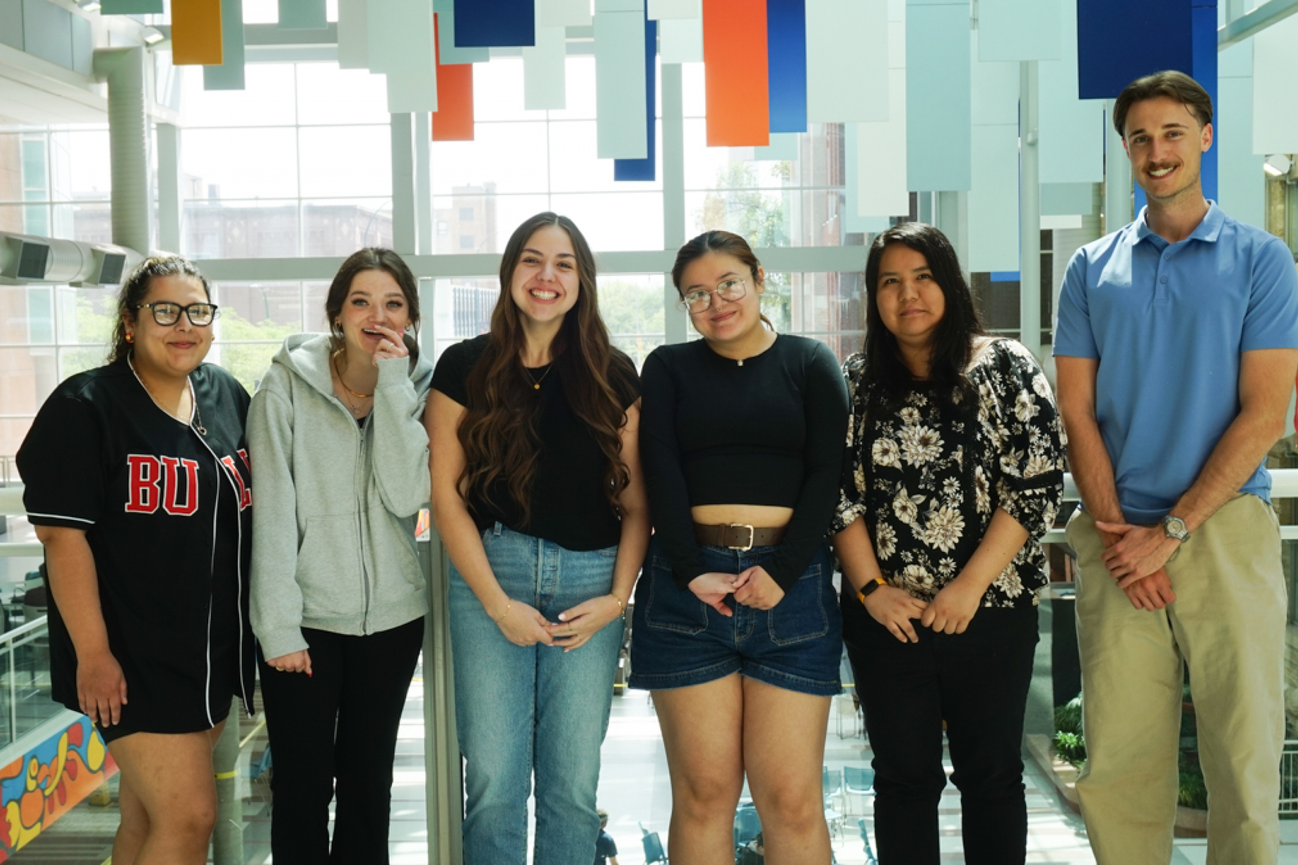 Six students in a large atrium with flags hanging from the ceiling.
