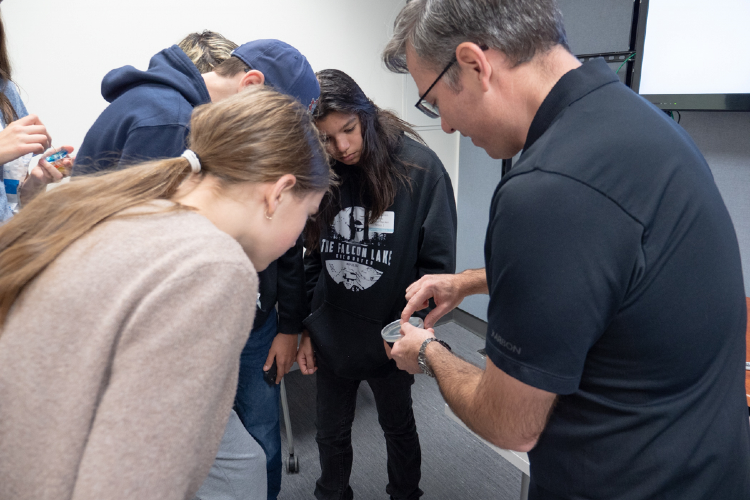 Three students observe a petri dish being shown by an educator.