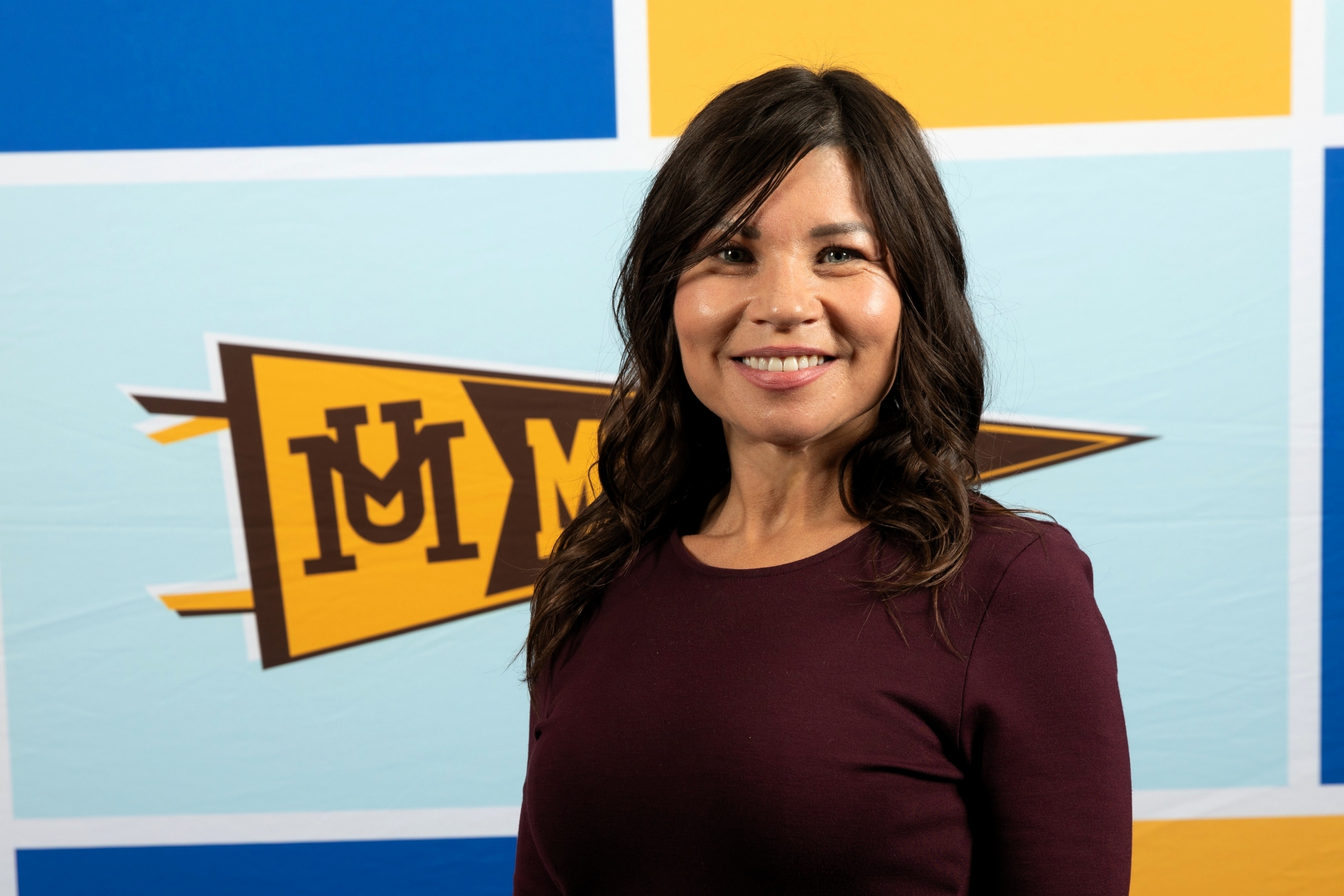 Tannis smiles in front of gold and blue UM branded backdrop. 
