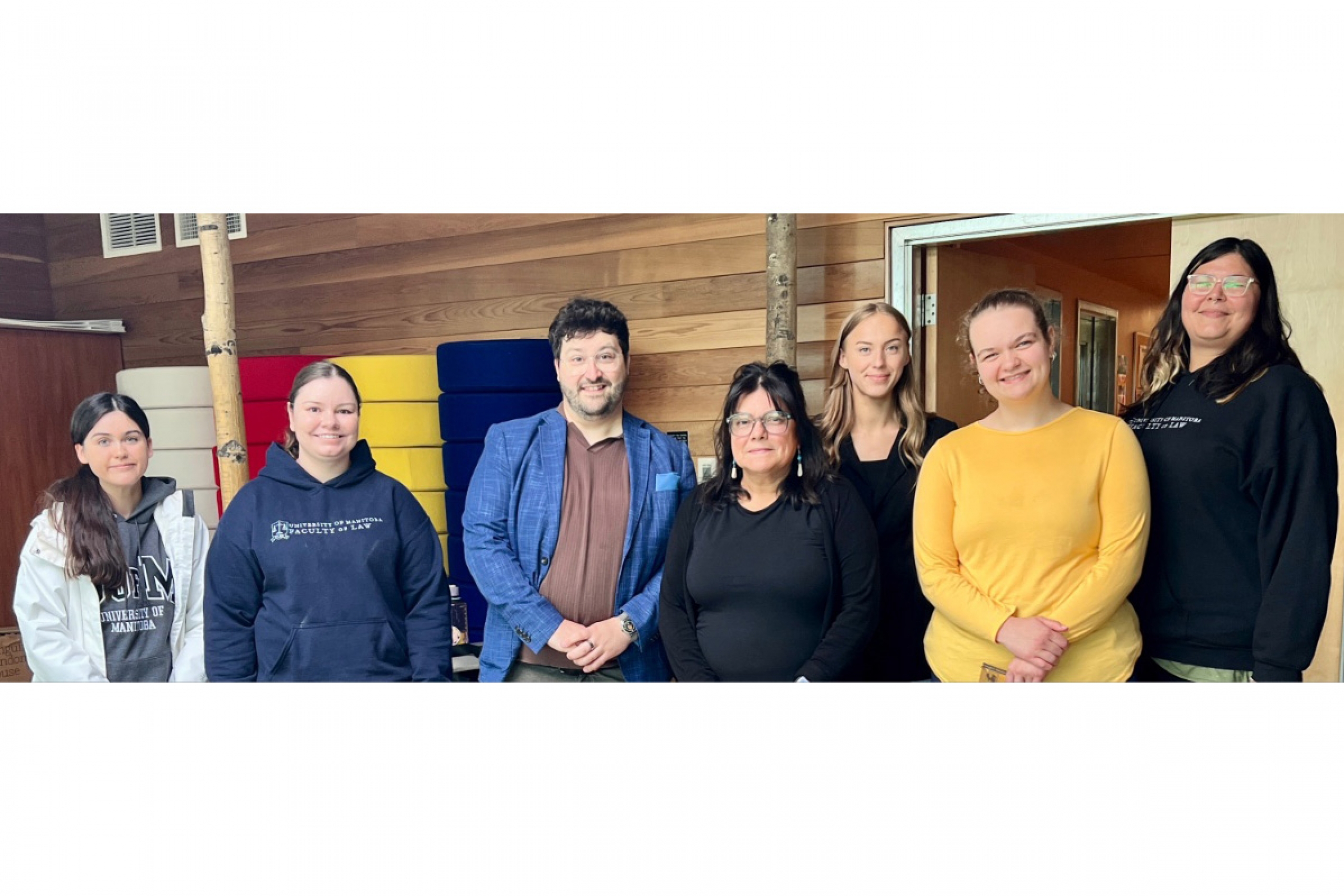 a group of people smile in front of a wood-paneled wall at the University college of the North