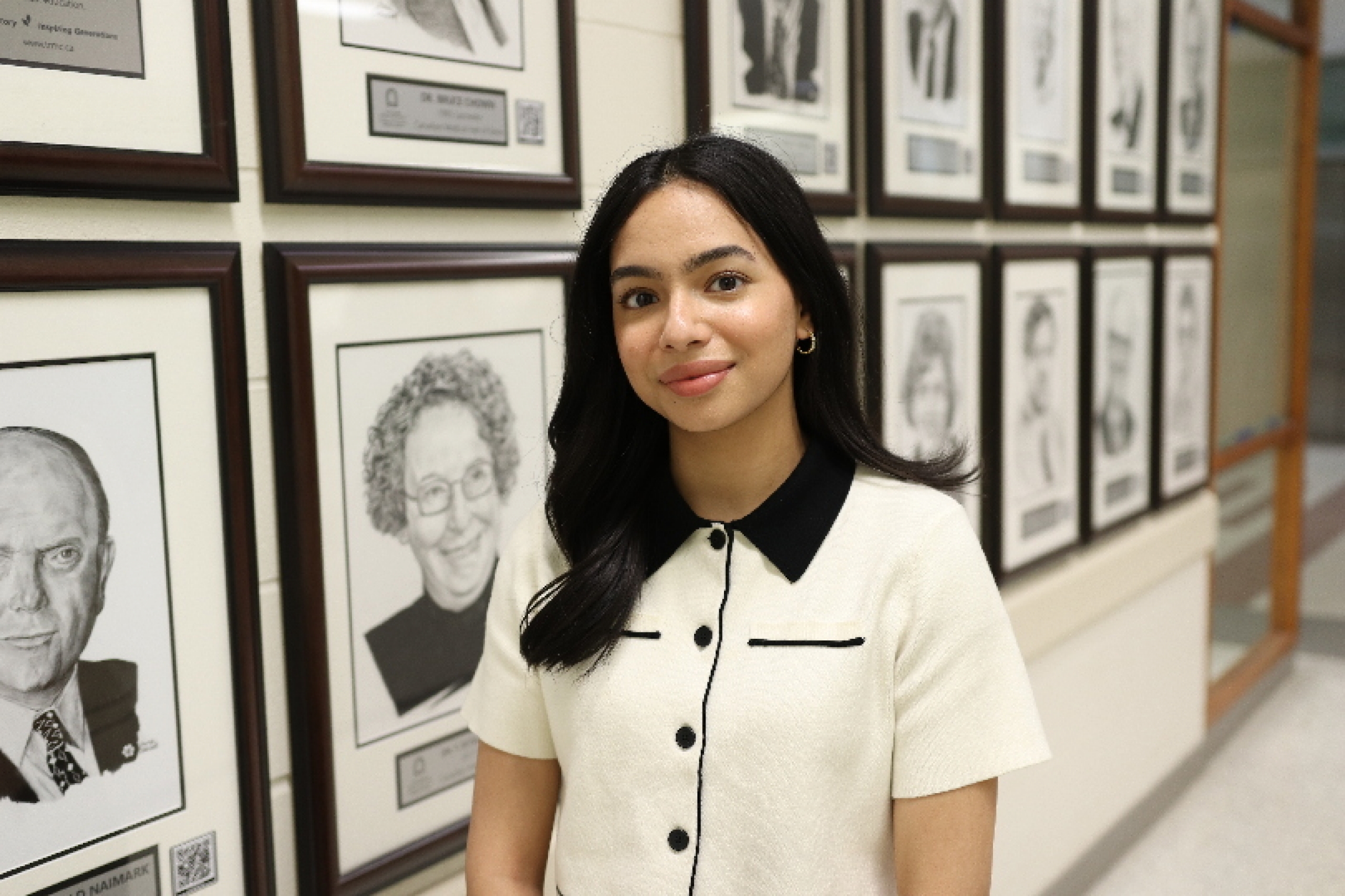 Tooba Razi stands in front of a wall of hand drawn head shots.