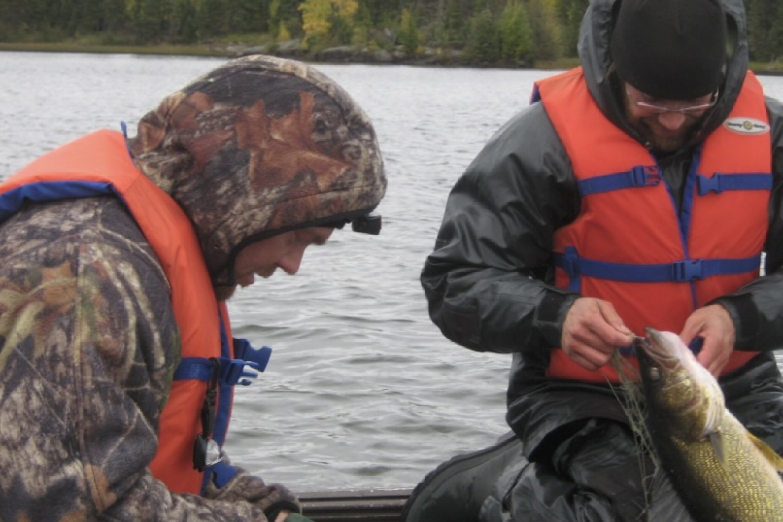 Two boaters out on a lake inspect a fish they've caught. 