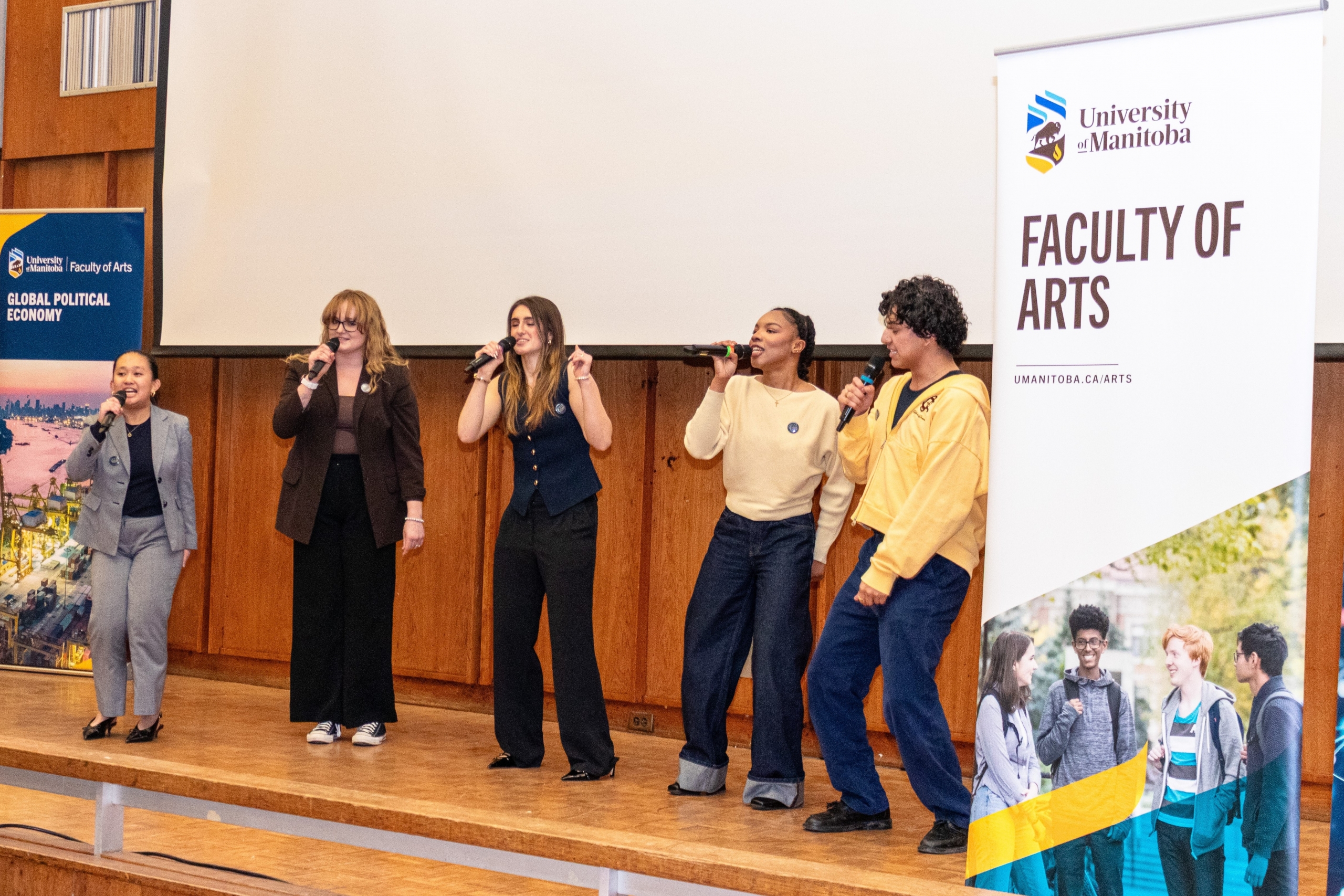 A group of 5 students, singing and dancing on stage. 