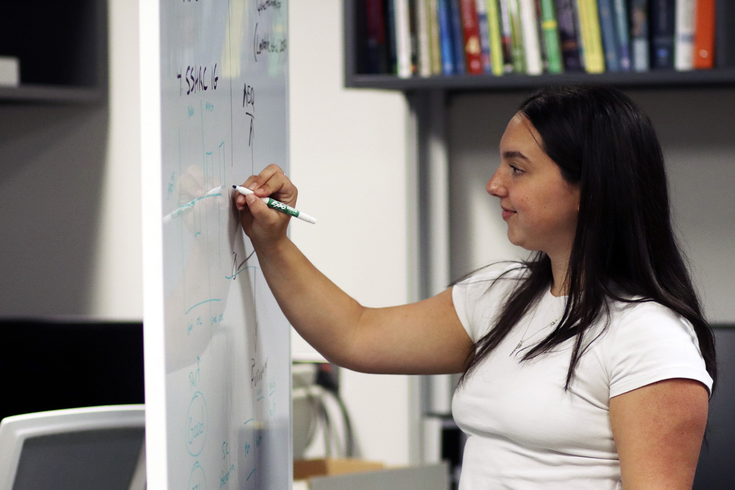 A young researcher writes on a whiteboard.
