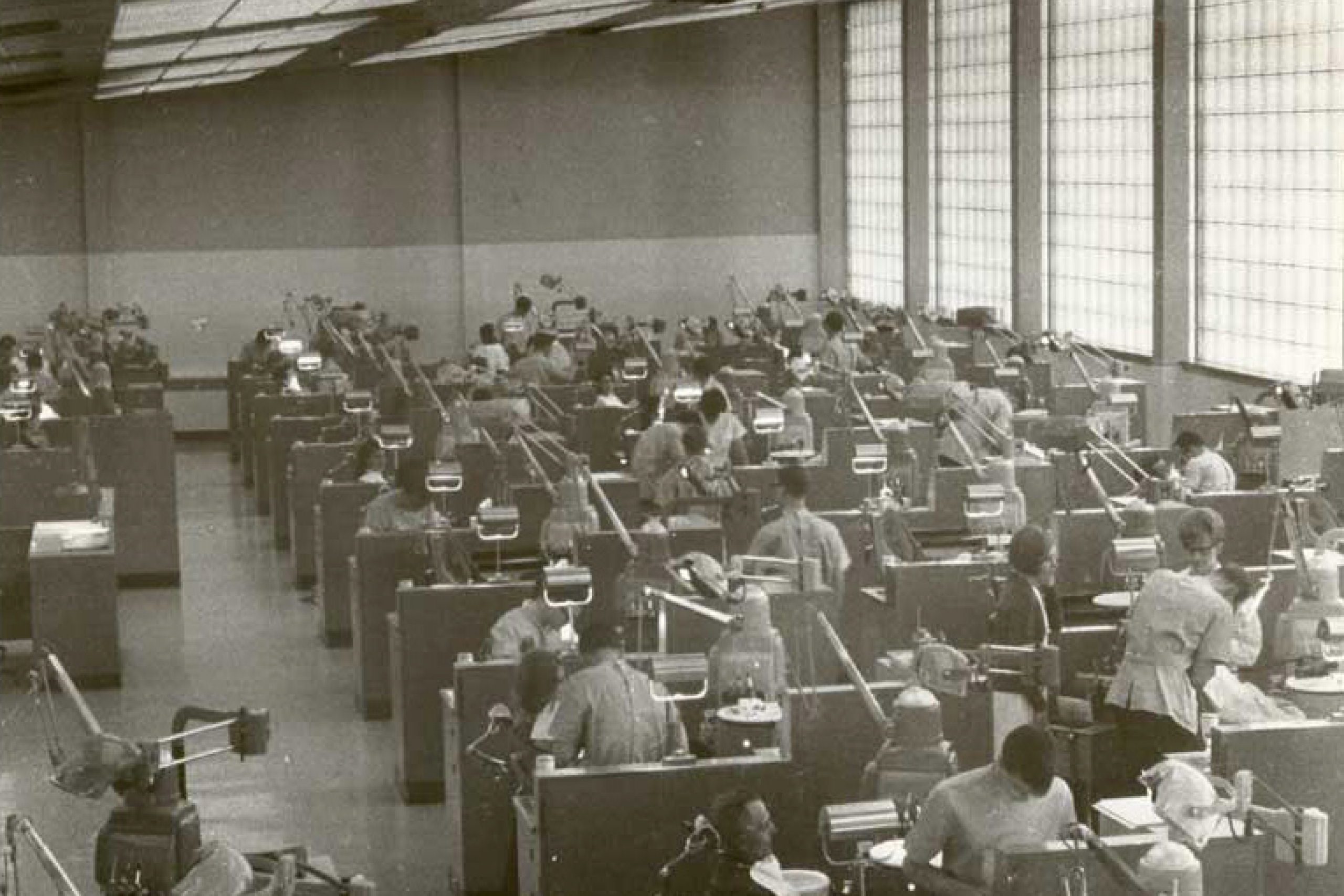 Black and white photo of the UM dental clinic with students working with patients sitting in dental chairs.
